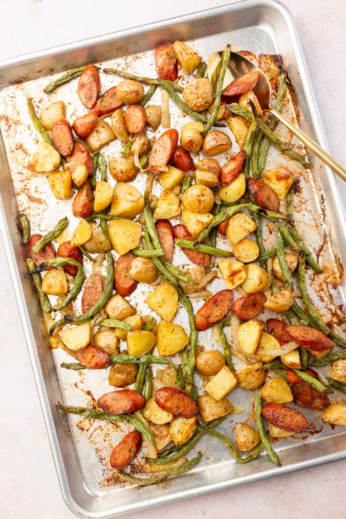A sheet pan filled with roasted potatoes, sausage, and green beans.