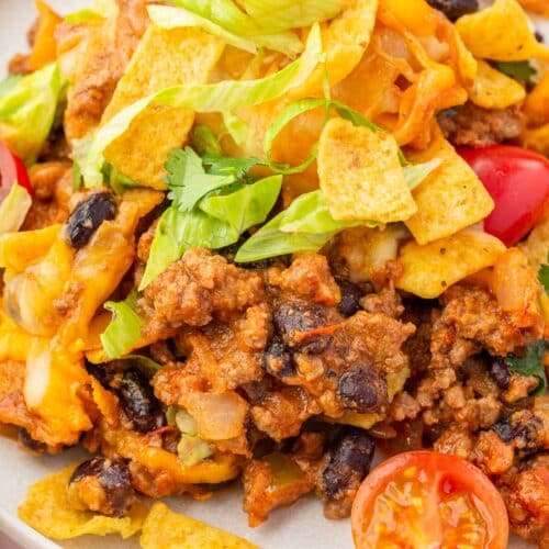 A white plate topped with Frito pie and corn chips.