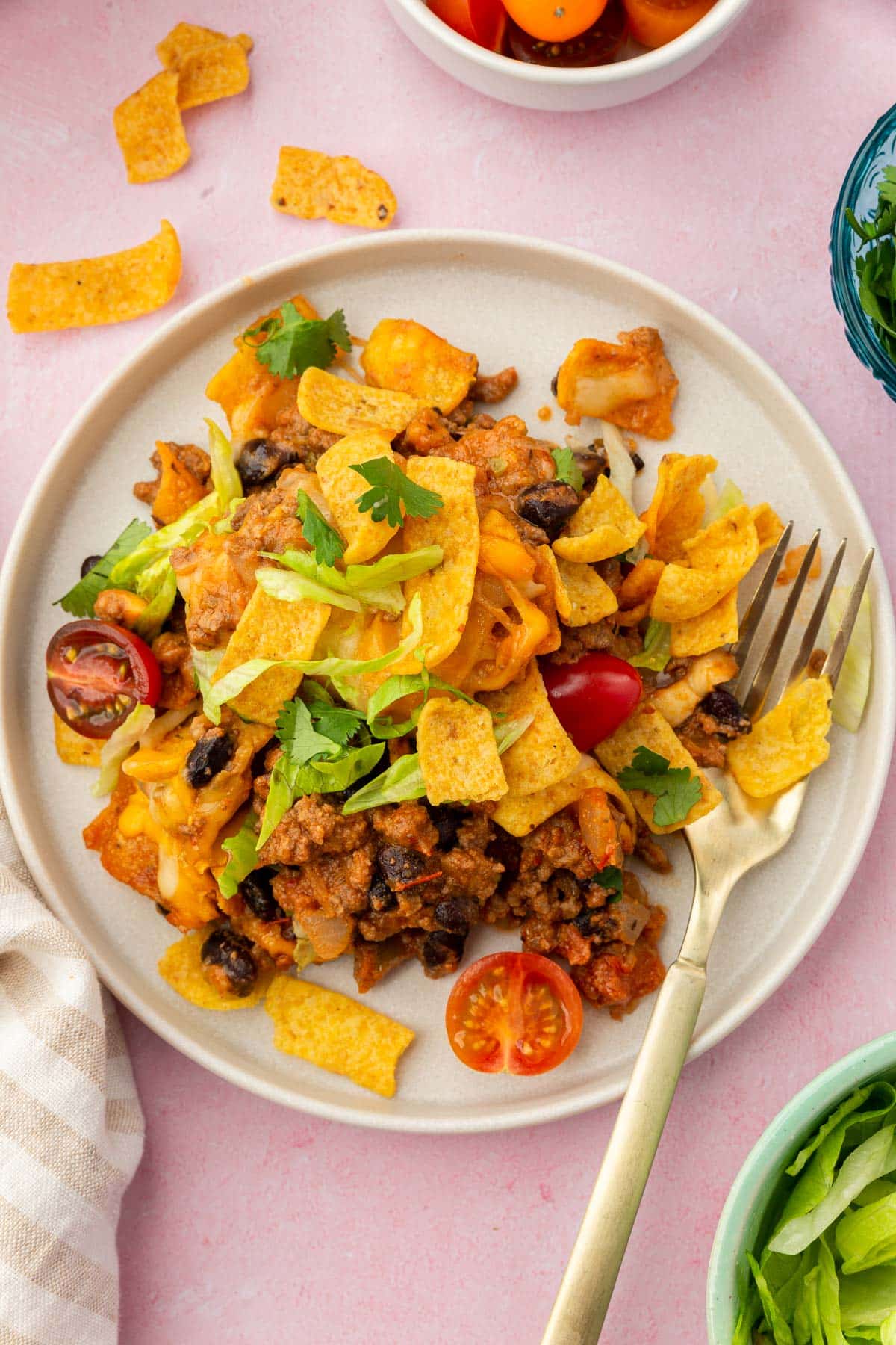 A white plate topped with a taco pie and a fork next to bowls of toppings like lettuce and tomatoes.