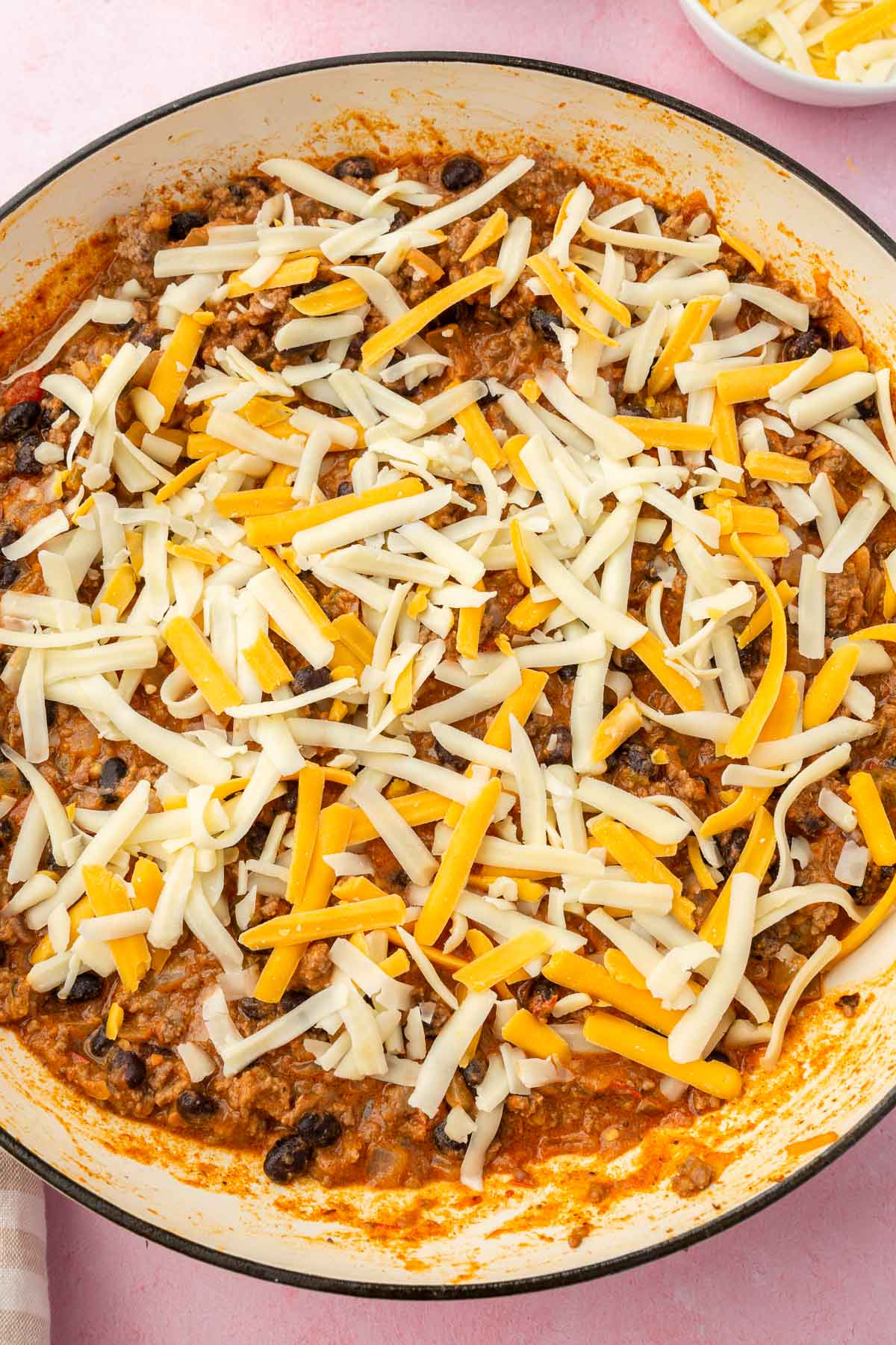 A skillet with cooked taco meat topped with shredded cheese before melting.