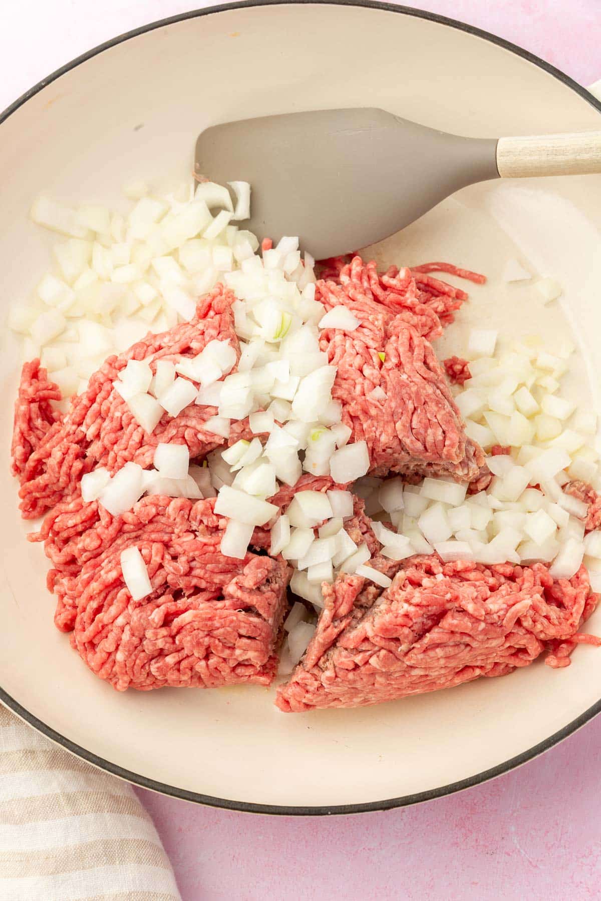 A white skillet filled with ground beef and diced onions before cooking.