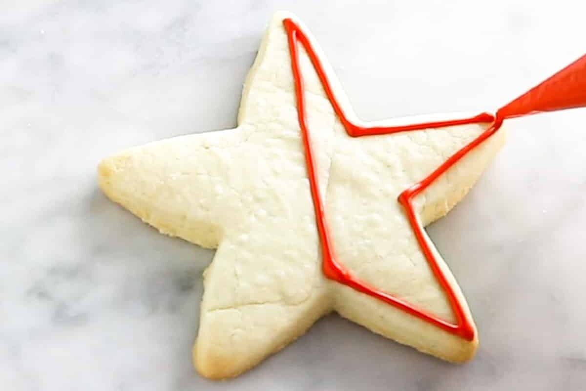 A star shaped sugar cookie that is being outlined with red royal icing.