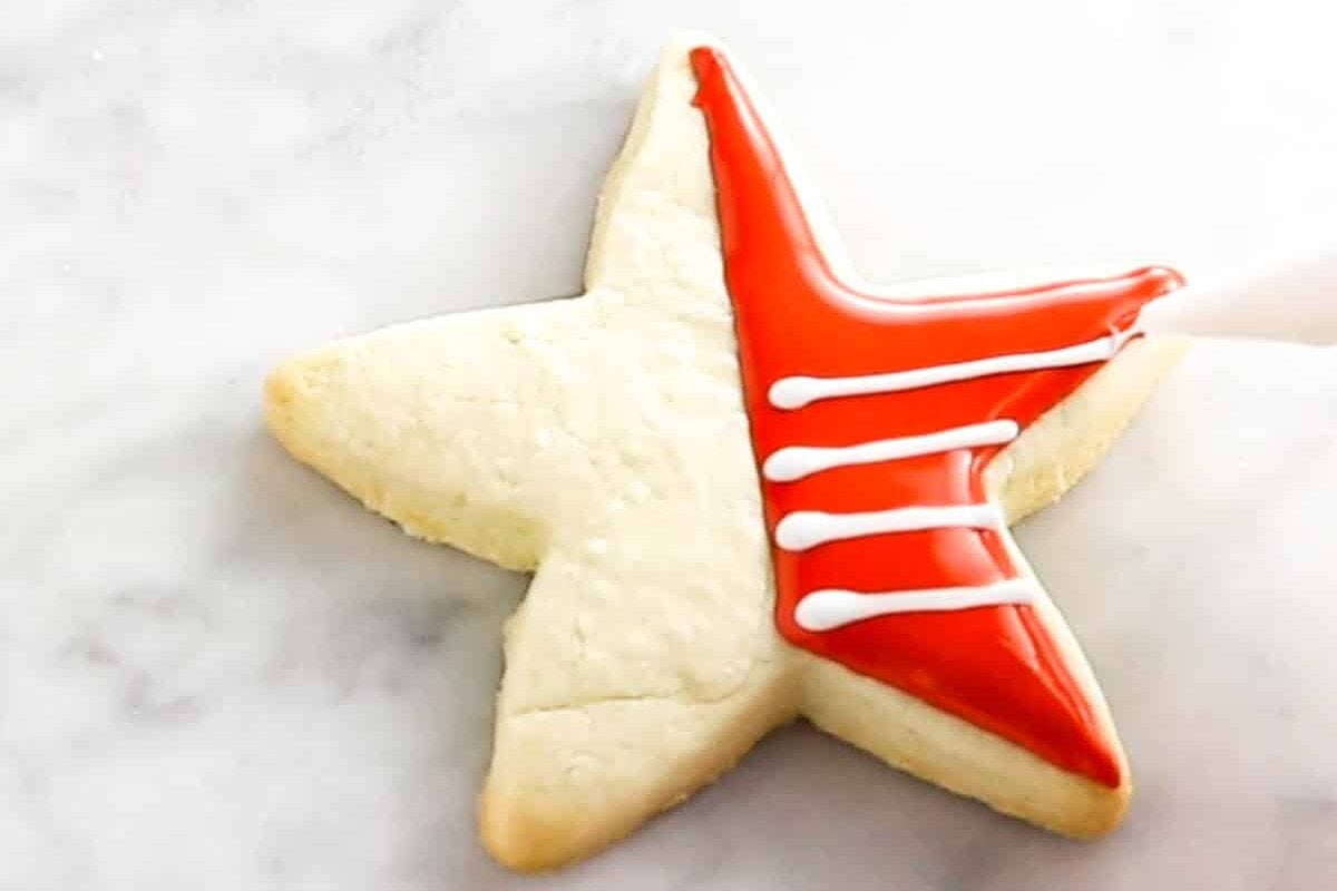 A star shaped sugar cookie that is being decorated with red royal icing and topped with white royal icing stripes.