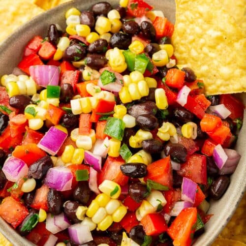 An overhead view of a bowl of tomato corn salsa with black beans on a platter of yellow tortilla chips.