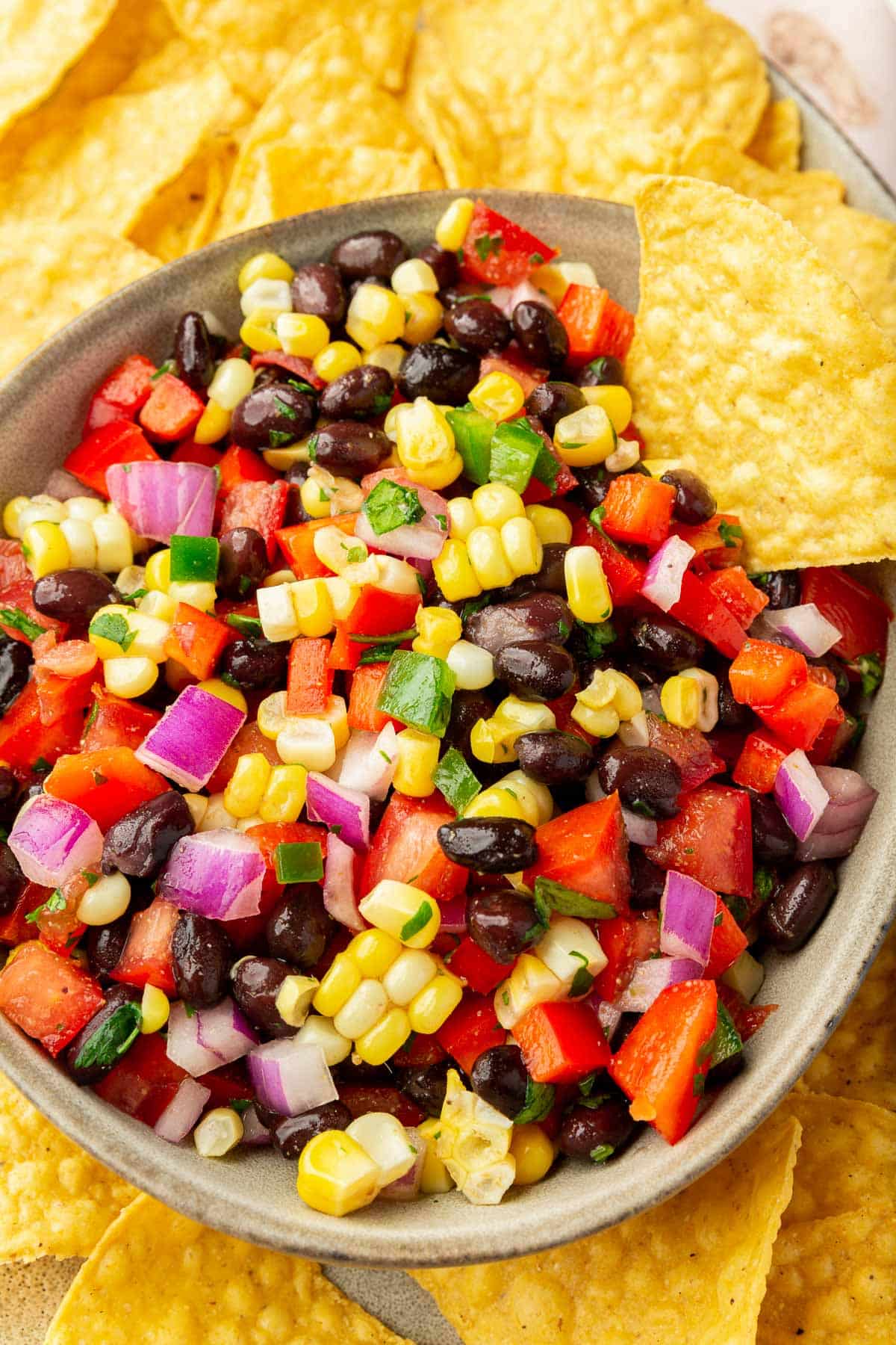 An overhead view of a bowl of tomato corn salsa with black beans on a platter of yellow tortilla chips.