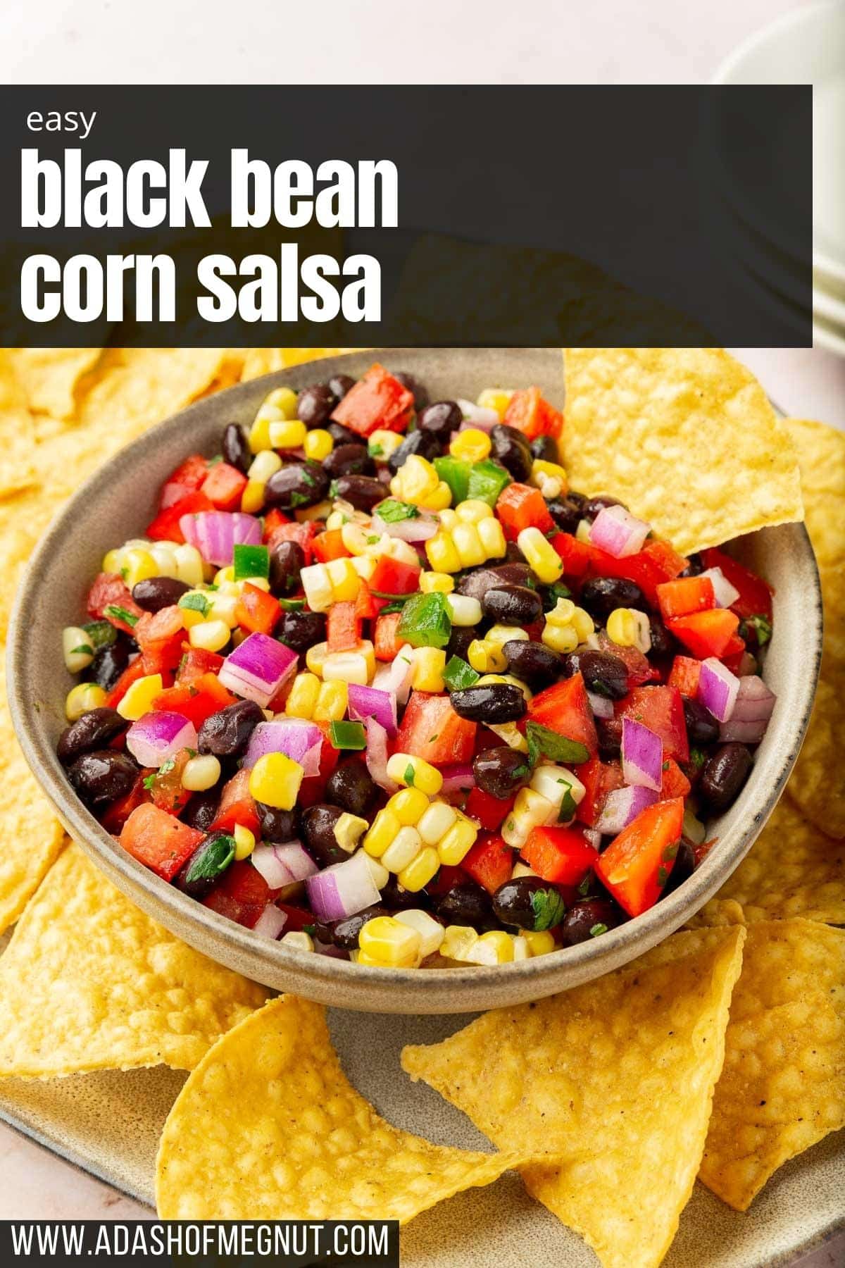 A bowl of a corn salsa with black beans and tomatoes on a platter of tortilla chips.