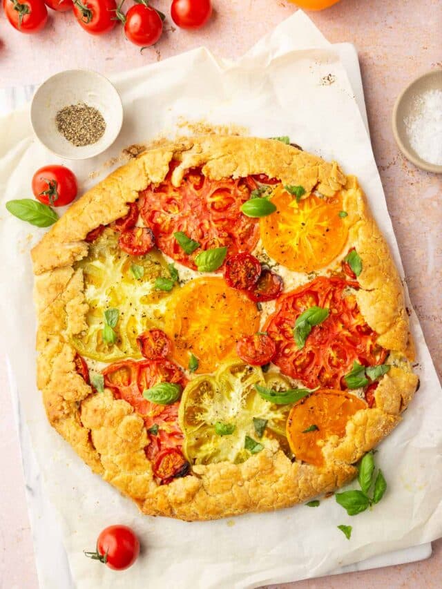 An overhead view of a gluten-free tomato galette topped with basil with cherry tomatoes to the side.