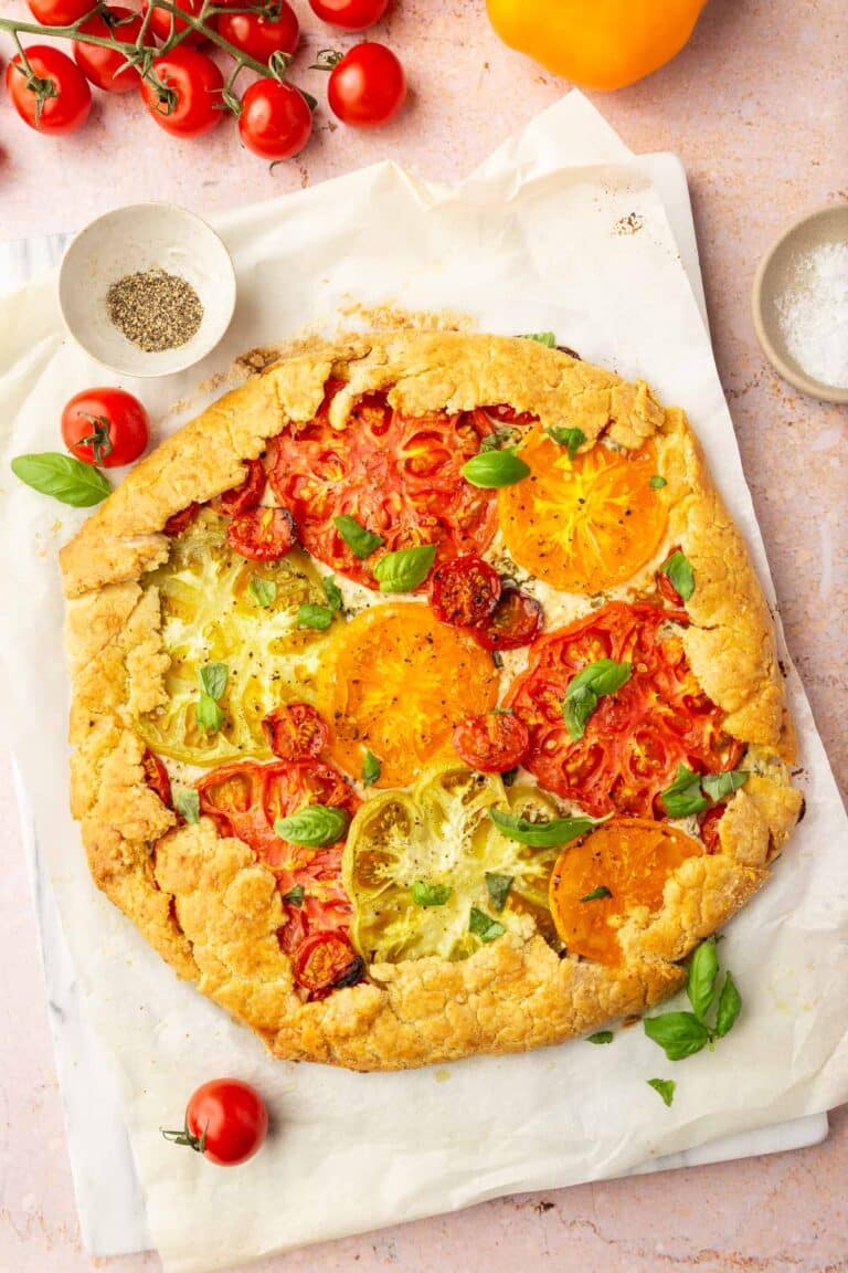 An overhead view of a gluten-free tomato galette topped with basil with cherry tomatoes to the side.