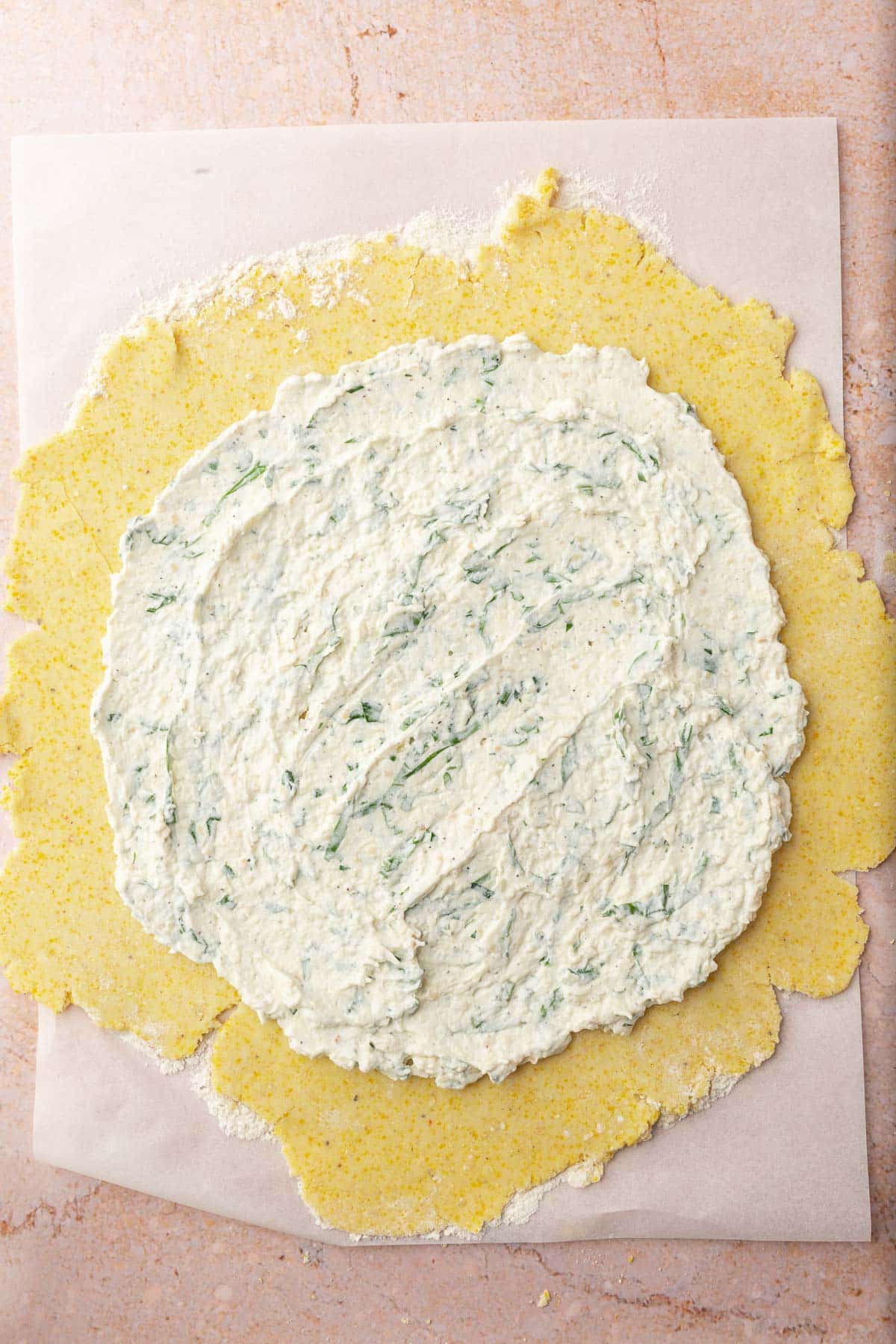 A ricotta herb mixture that has been spread over a round piece of gluten-free tart dough to make a tomato galette.