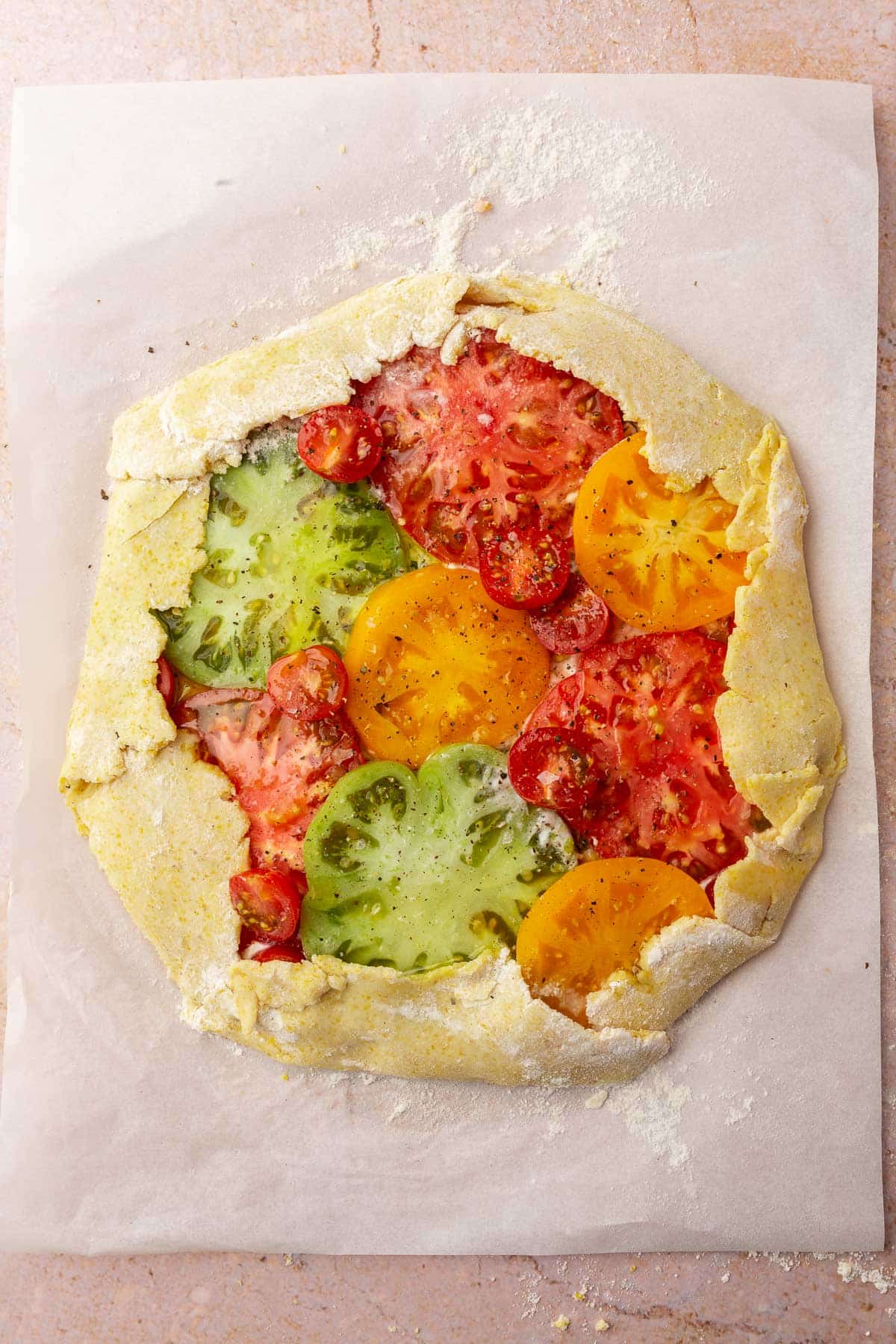 A raw tomato galette on a piece of floured parchment paper.