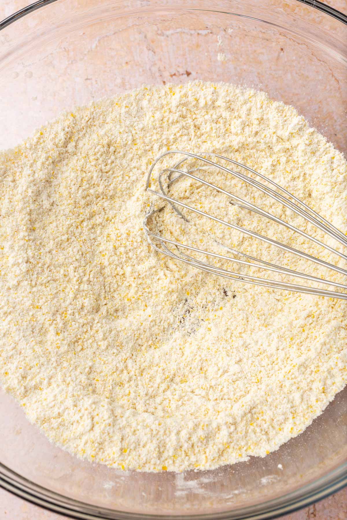 A glass bowl with a gluten-free flour mixture and a wire whisk.