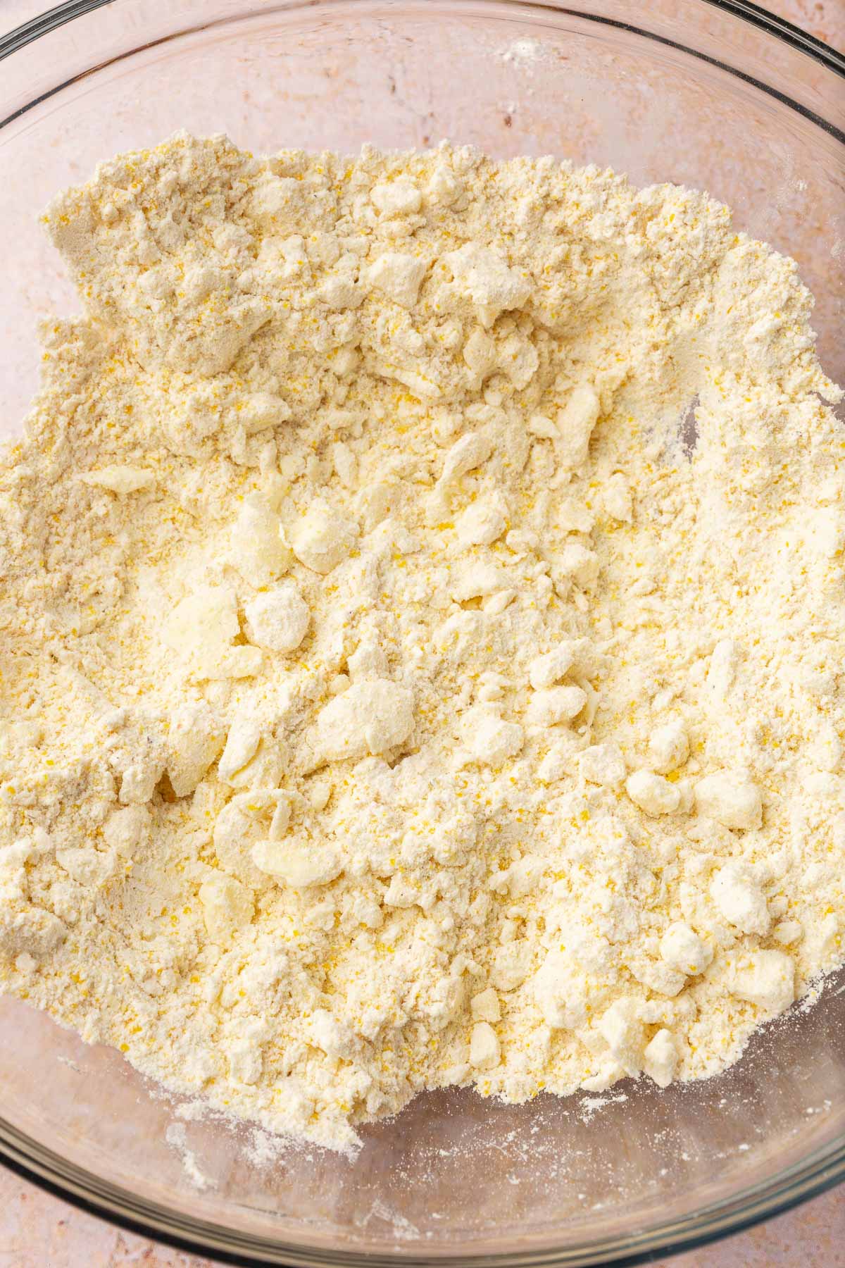 A glass mixing bowl with a gluten-free flour mixture tossed with small bits of cold butter.