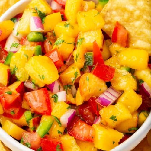 A close up of a bowl of peach mango salsa with tomatoes with tortilla chips surrounding the bowl.