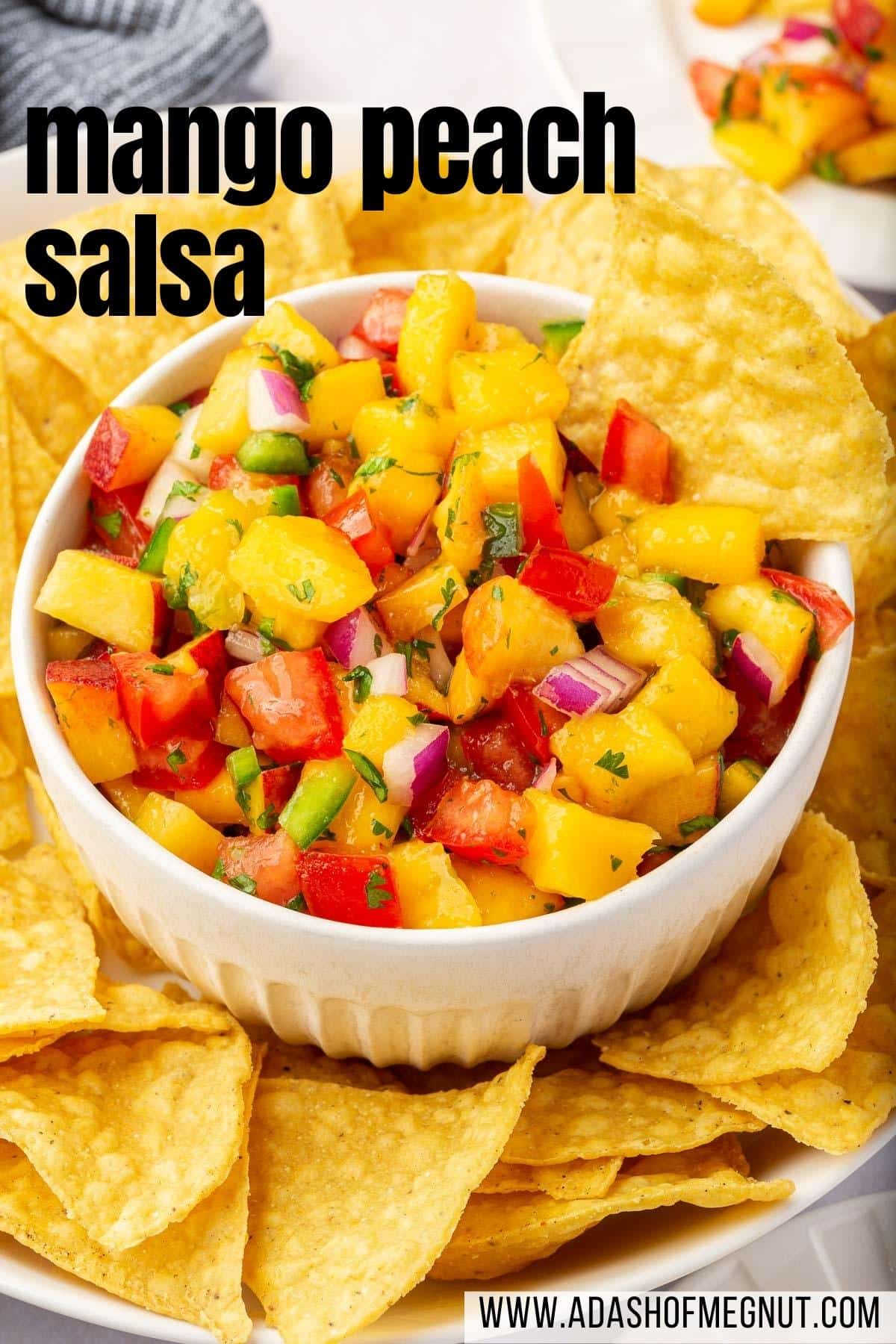 A bowl of peach mango salsa with tomatoes on a plate of tortilla chips.