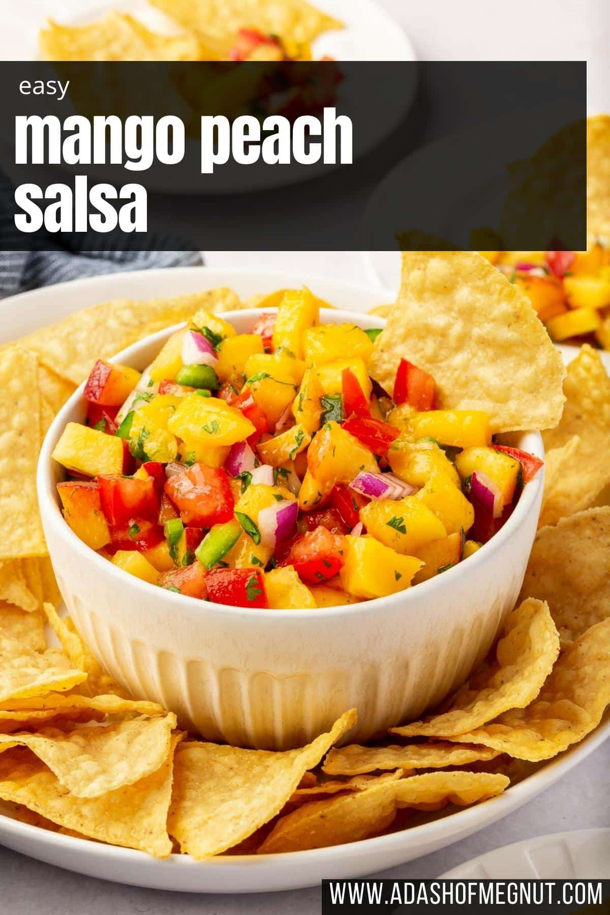 A bowl of mango peach salsa in a larger bowl of tortilla chips with appetizer plates in the background.