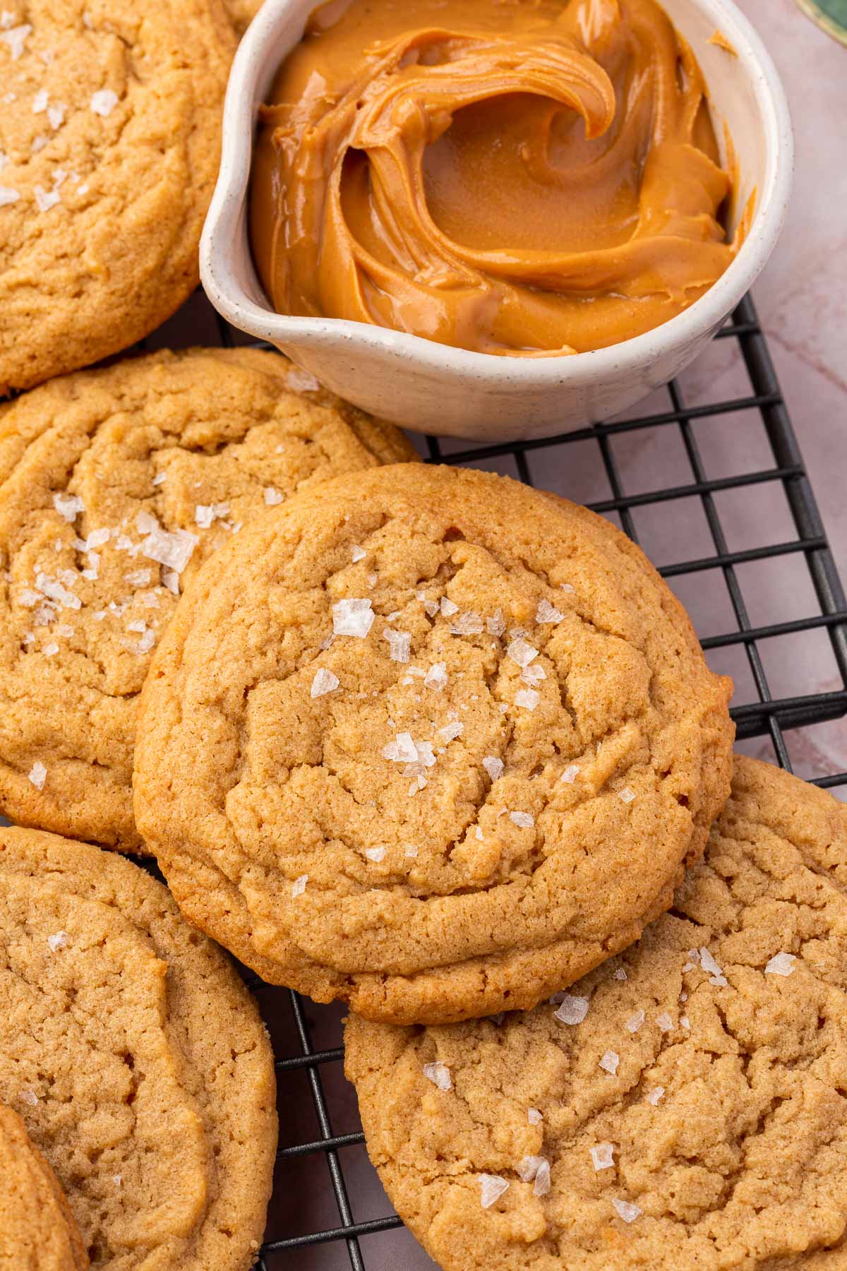 Gluten-free peanut butter cookies on a wire cooling rack with a small bowl of peanut butter to the side.