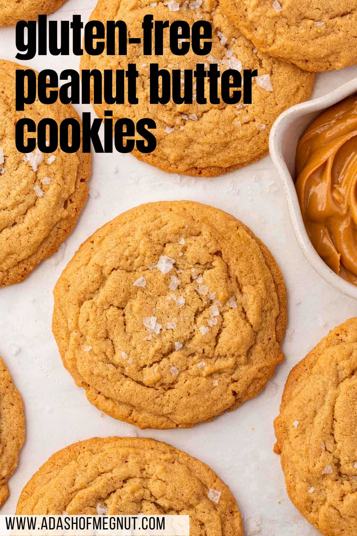 An overhead view of gluten free peanut butter cookies on a piece of parchment paper with a bowl of peanut butter to the side.