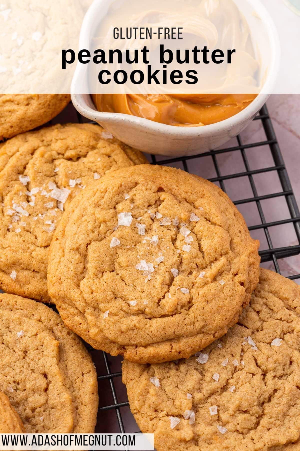 Stacks of glutenfree peanut butter cookies cooling on a wire rack and topped with flaky sea salt.