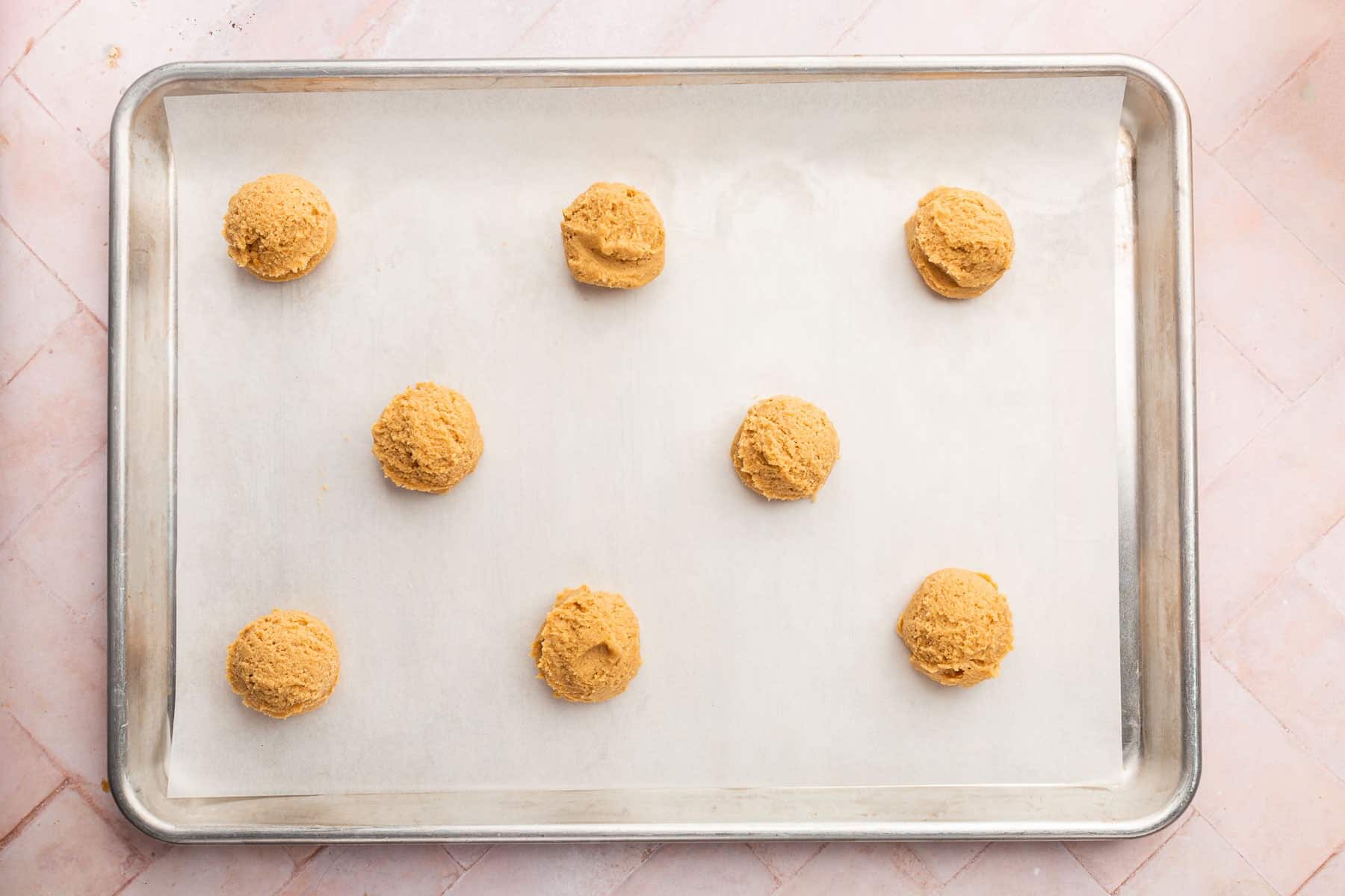 Eight balls of gluten-free peanut butter cookie dough on a baking sheet lined with parchment paper.