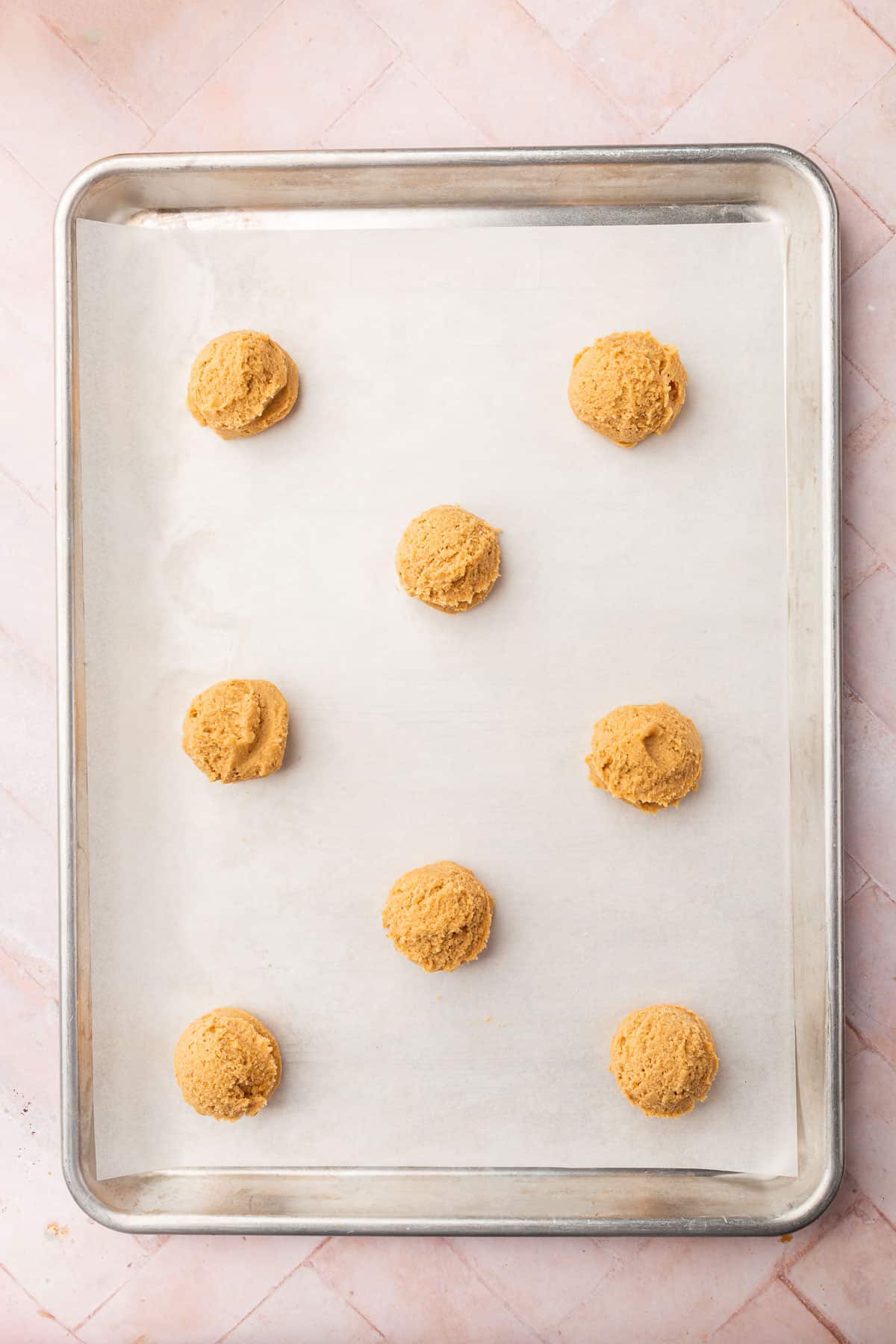 Eight balls of gluten-free peanut butter cookie dough on a baking sheet lined with parchment paper.