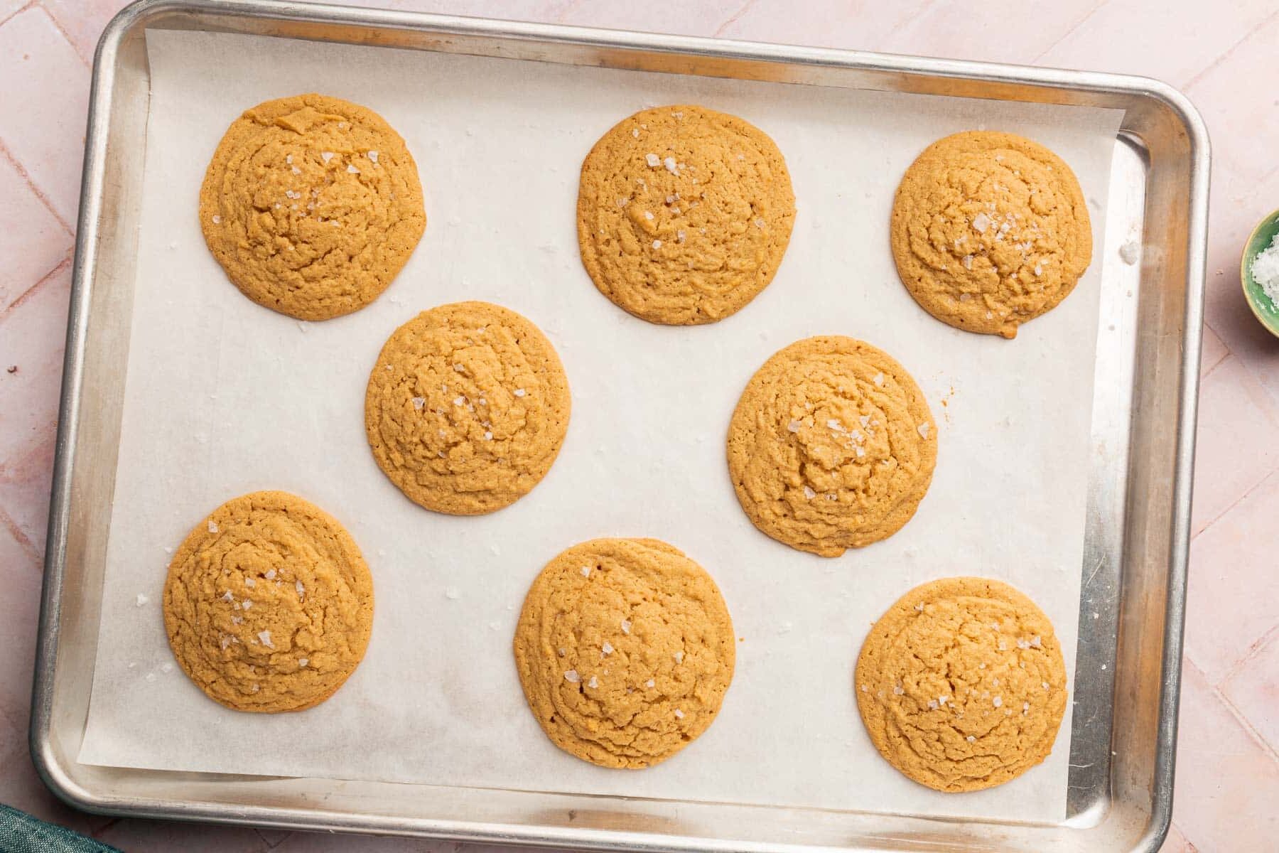 Eight gluten-free peanut butter cookies on a baking sheet lined with parchment paper.