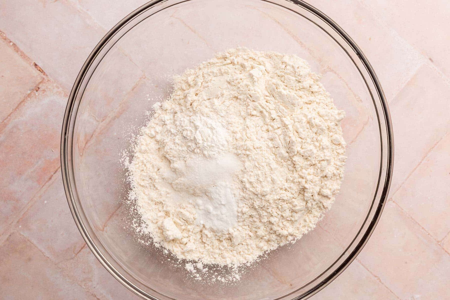 A glass mixing bowl with gluten-free flour, baking soda, baking powder, and salt in it.