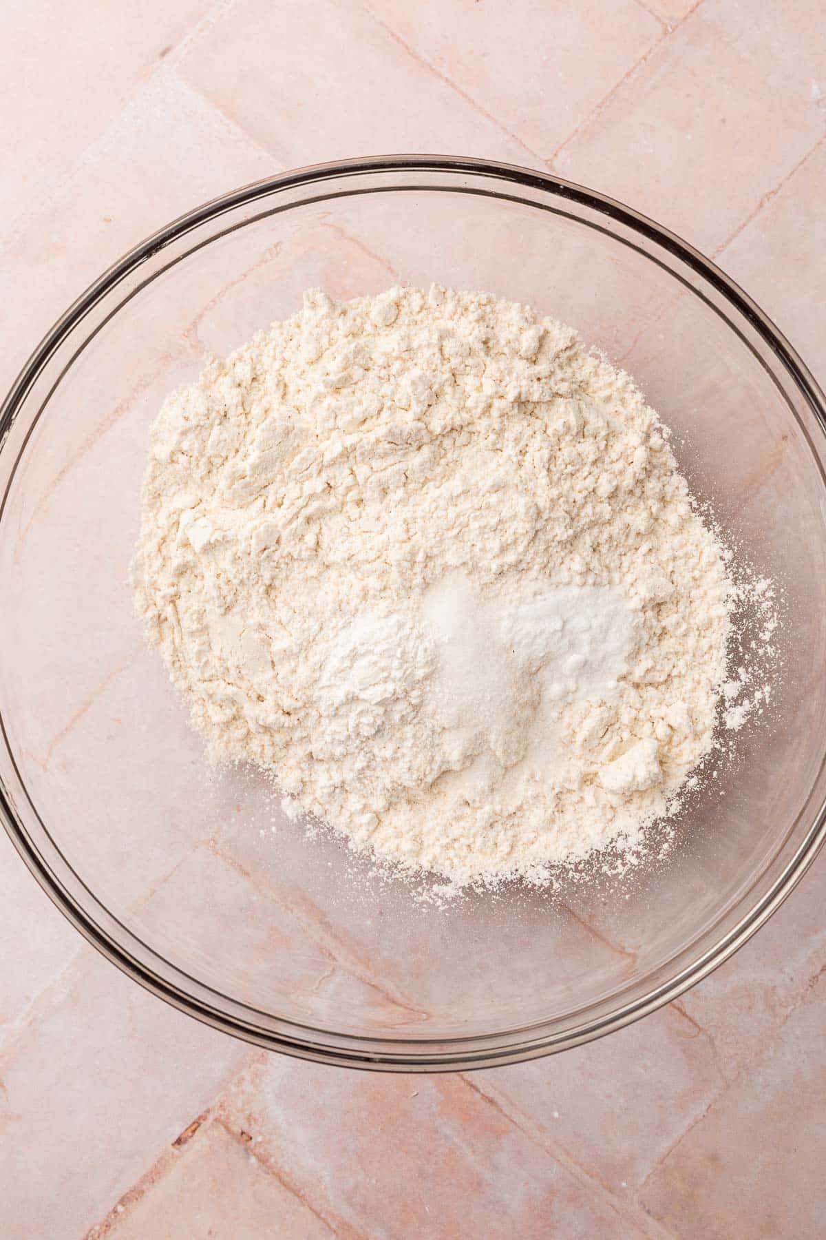 A glass mixing bowl with gluten-free flour, baking soda, baking powder, and salt in it.