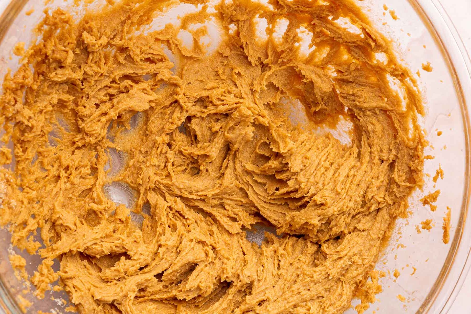 A glass mixing bowl with a creamed peanut butter and sugar mixture in it.