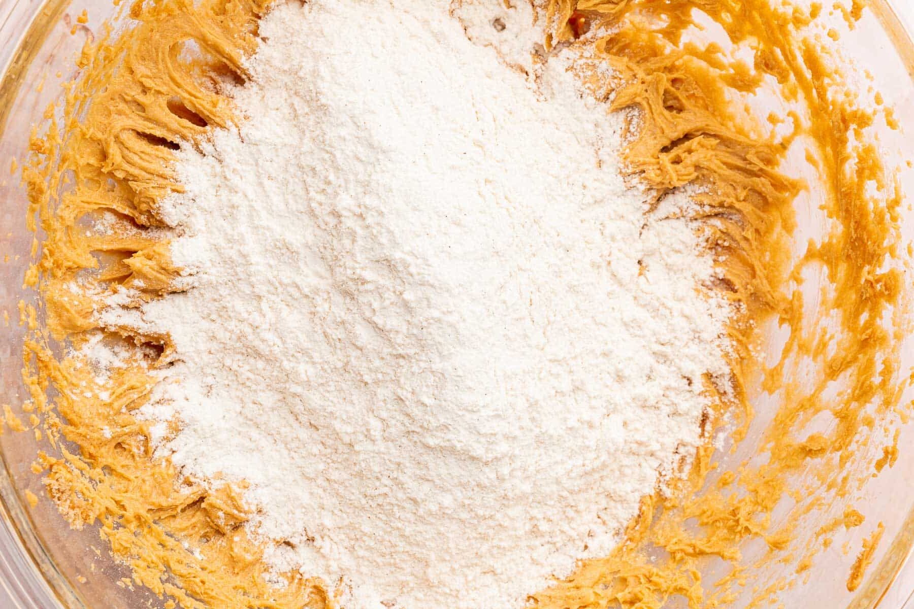 A glass mixing bowl with a peanut butter mixture topped with a gluten-free flour mixture before mixing together.