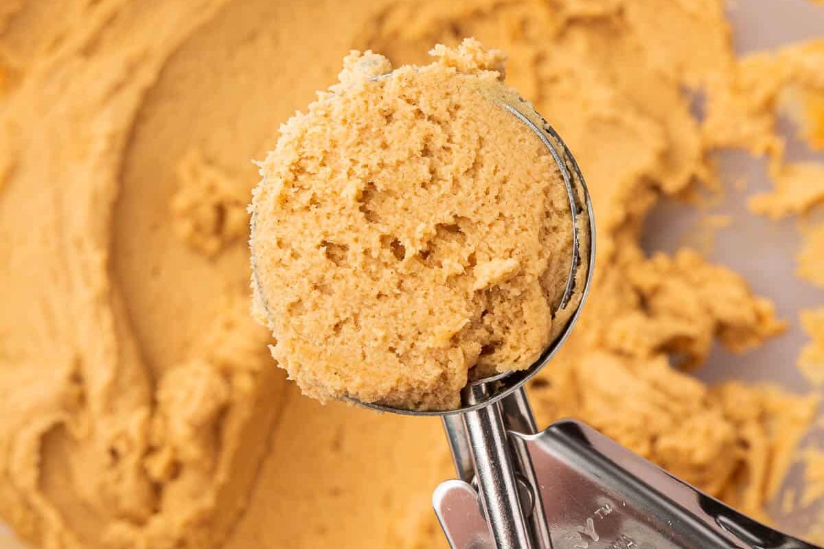 A cookie scoop with peanut butter cookie dough in it over a bowl of additional cookie dough.