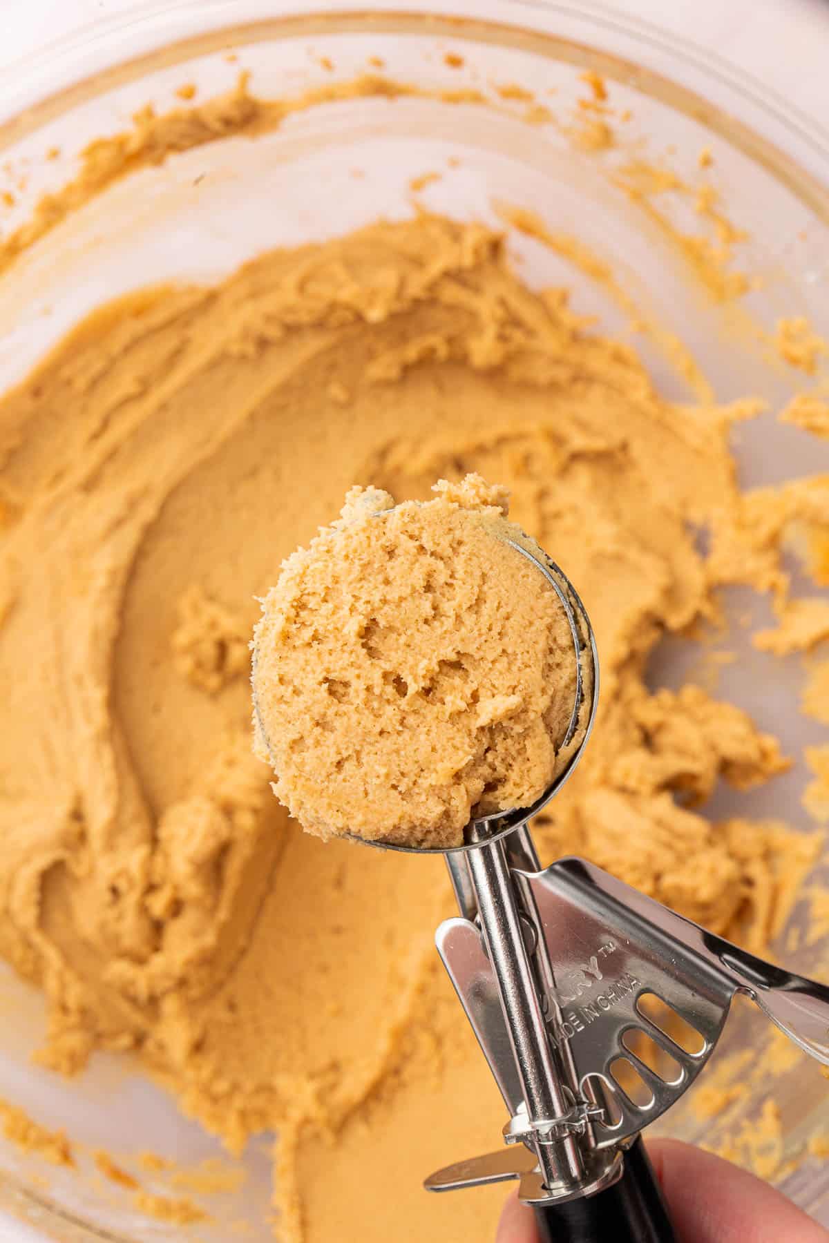 A cookie scoop with peanut butter cookie dough in it over a bowl of additional cookie dough.