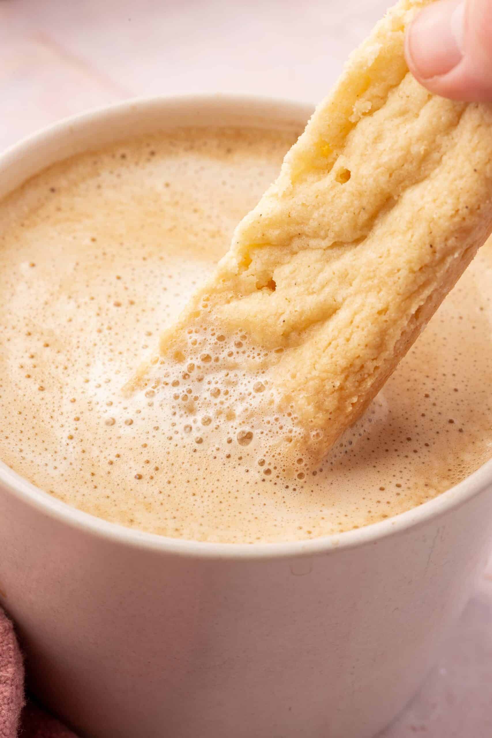 A close up of a slice of gluten-free shortbread being dipped into a latte.