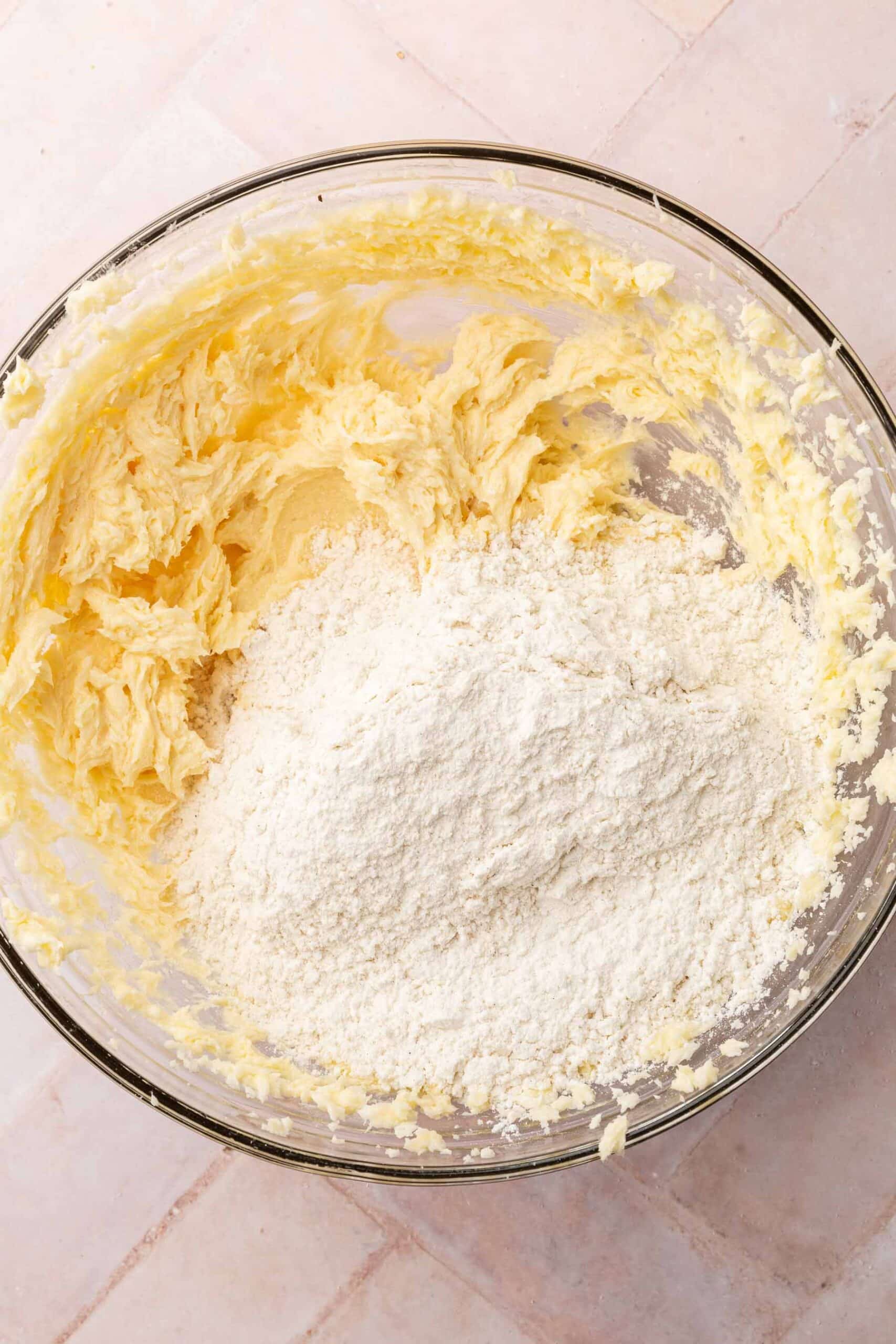 A glass mixing bowl with creamed butter and sugar topped with a gluten-free flour blend.