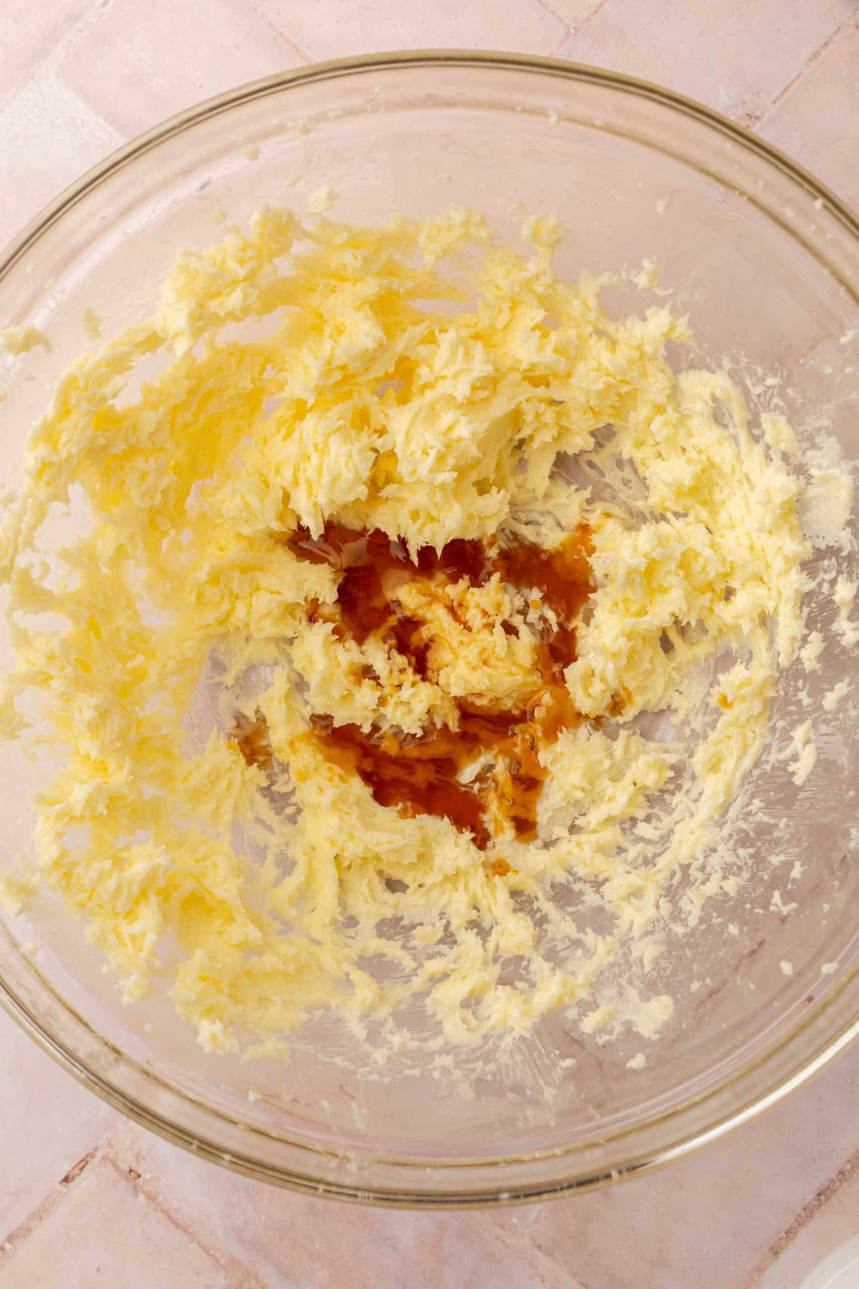 A glass mixing bowl with creamed butter and sugar topped with vanilla extract.