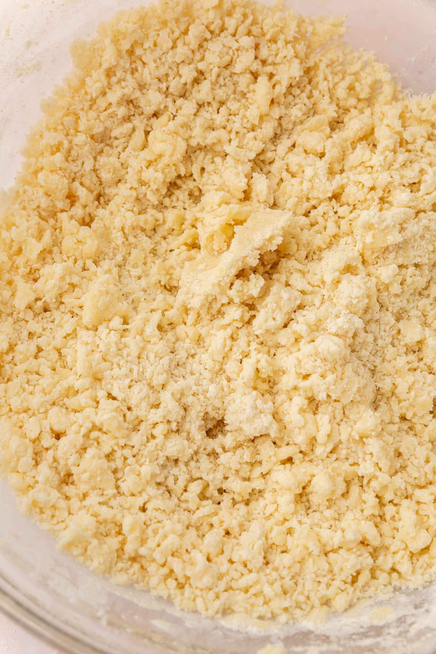 A close up of crumbly gluten-free shortbread dough in a glass mixing bowl.