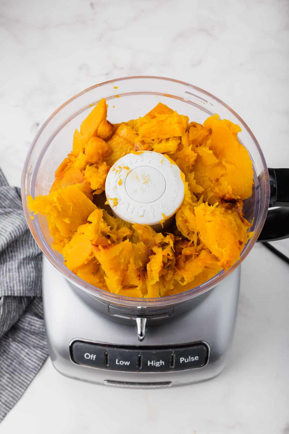 A food processor with chunks of roasted pumpkin in it before pureeing together.
