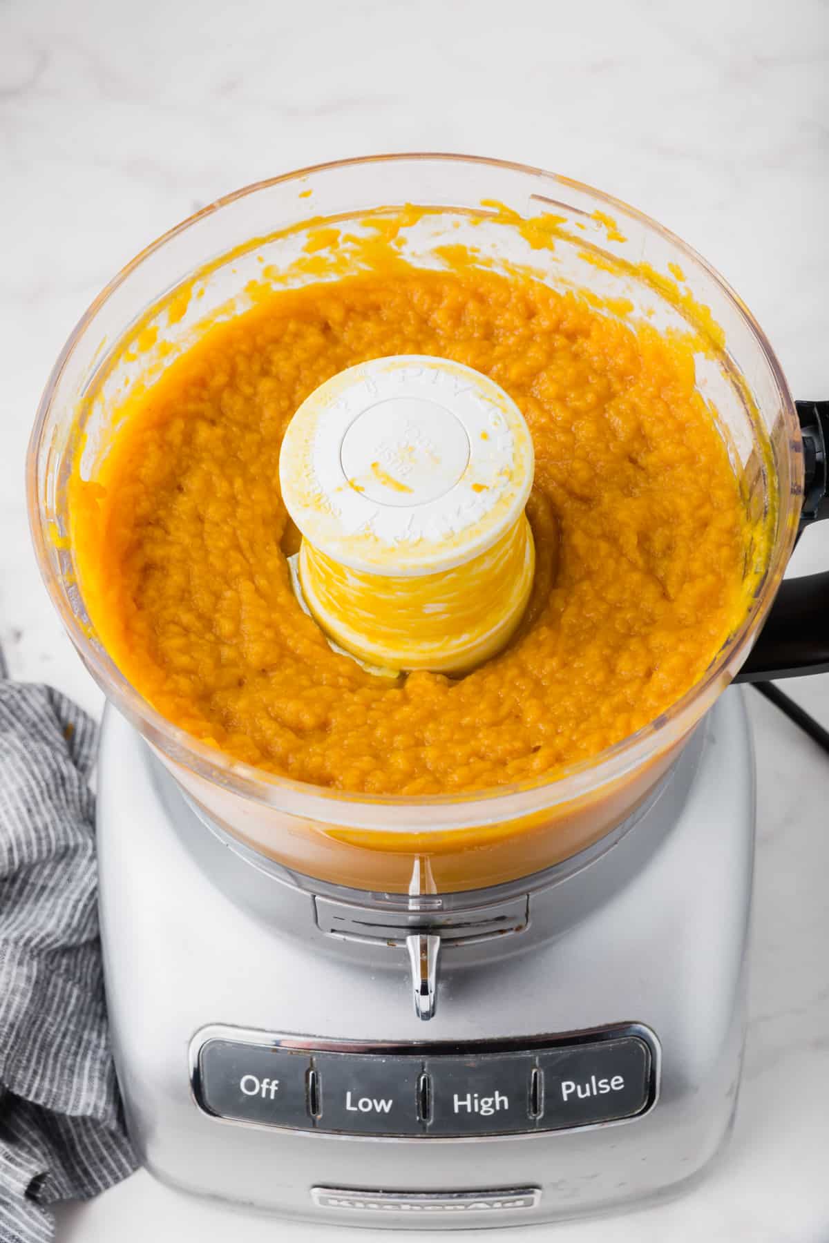 A food processor with pureed pumpkin in it.