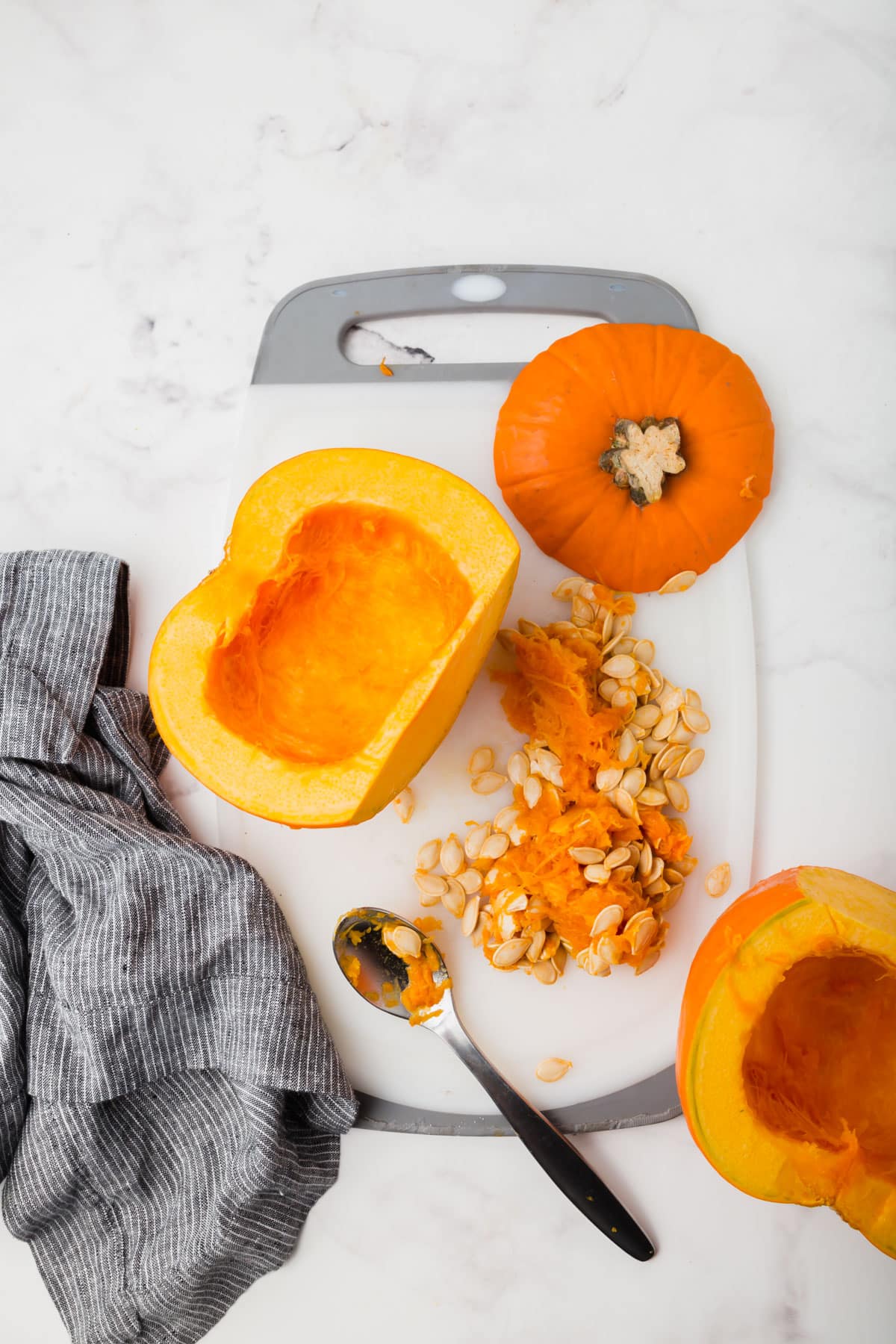 A cutting board with a sugar pumpkin cut in half with the seeds and pulp scooped out of the halves.