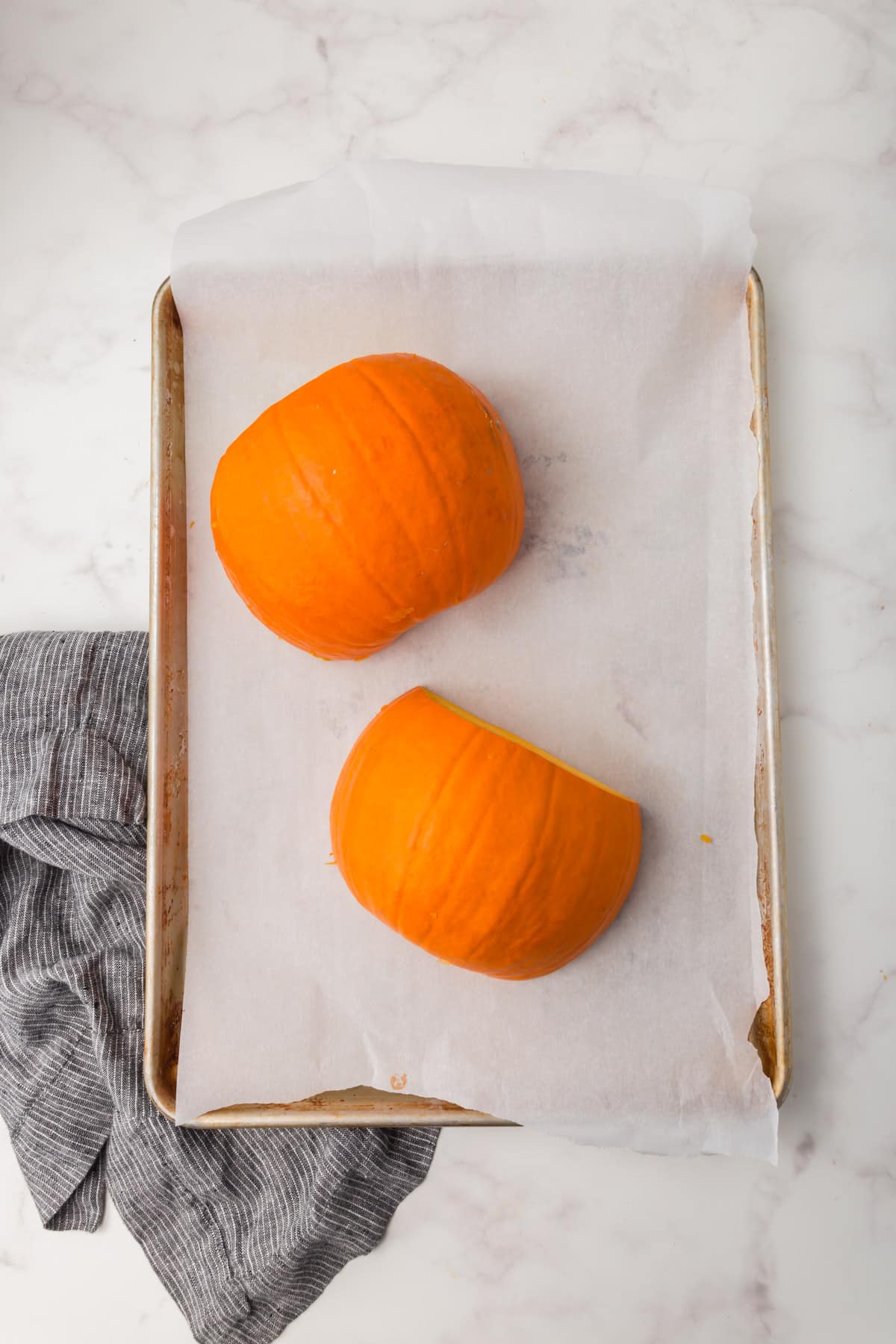 A baking sheet lined with parchment paper with two sugar pumpkin halves on it before cooking in the oven.