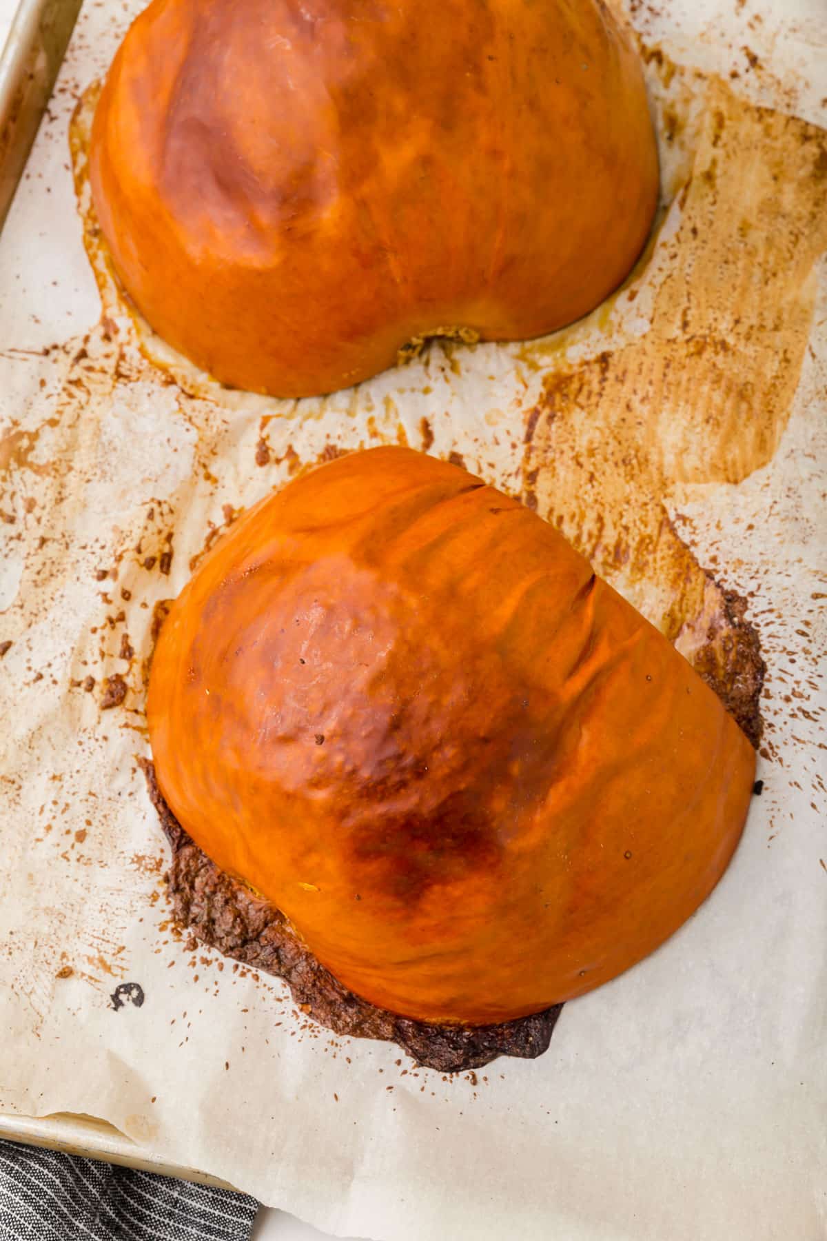 A sheet pan lined with parchment paper with two roasted pumpkin halves on it.