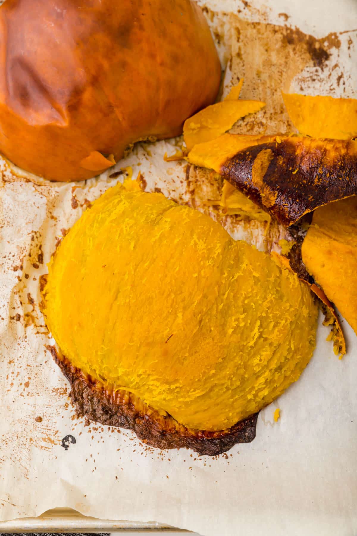 Two roasted pumpkin halves on a piece of parchment paper, with one of the halves having the skin peeled off.