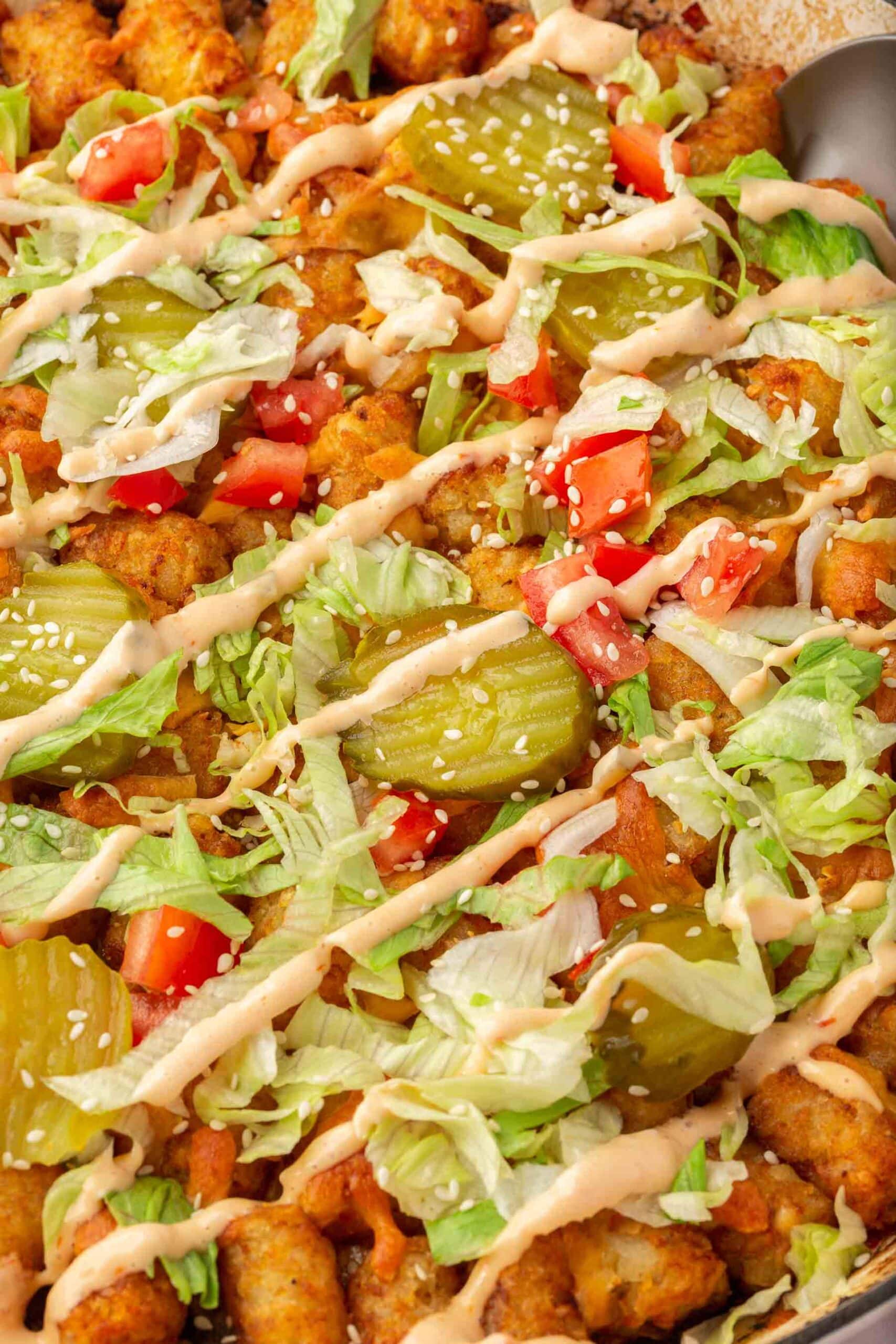 A close up of a big mac casserole with pickles, lettuce, tomatoes, and big mac sauce in a casserole dish.