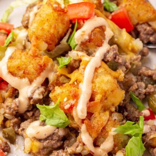 A close up of a single serving of big mac casserole with tater tots and ground beef on a salad plate with a fork.