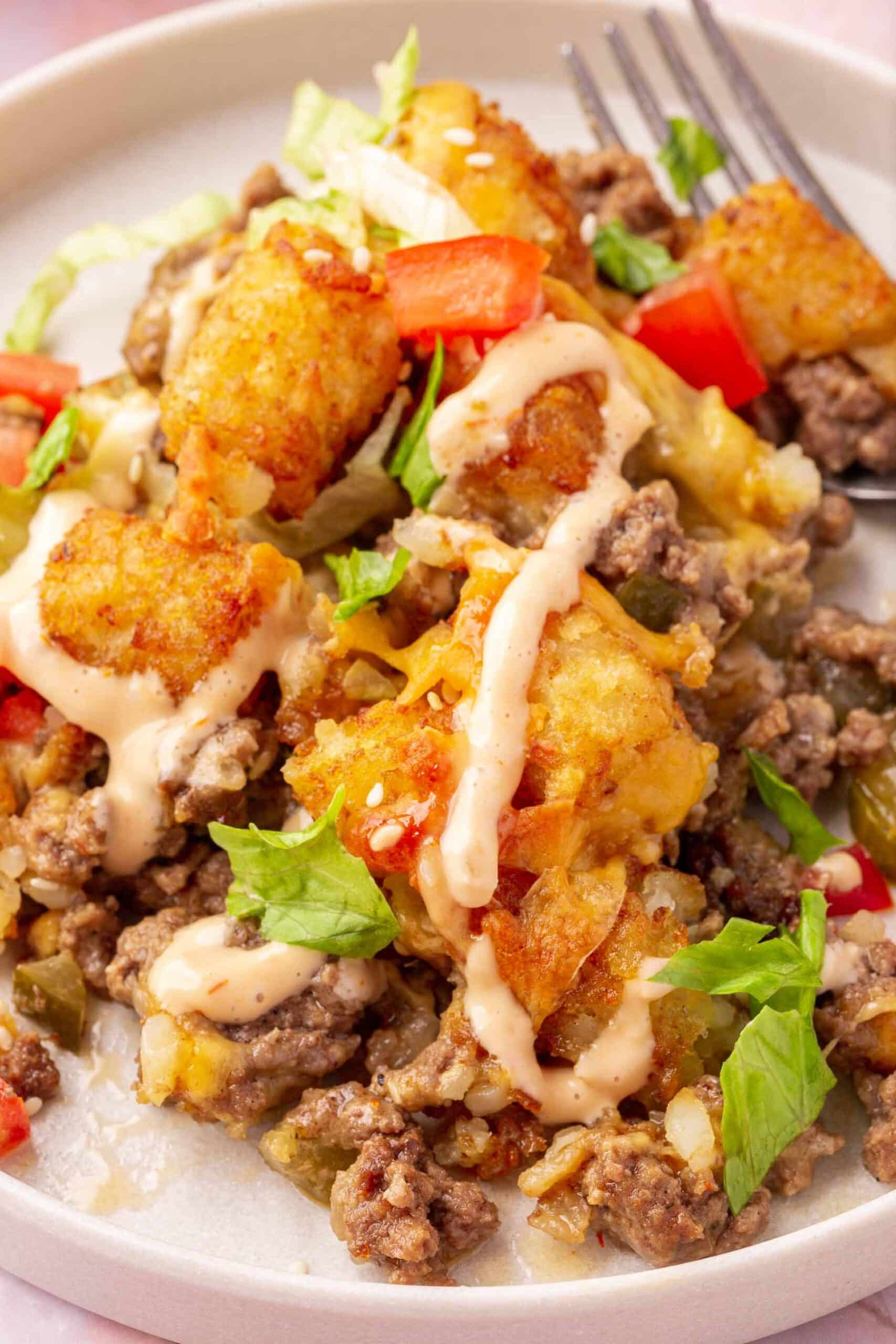 A close up of a single serving of big mac casserole with tater tots and ground beef on a salad plate with a fork.