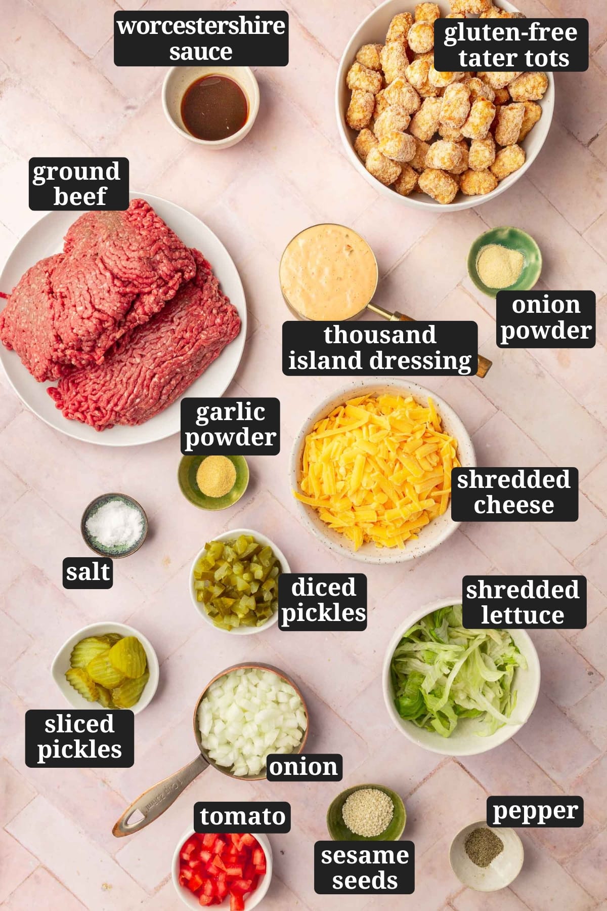 An overhead view of ingredients in bowls to make big mac tater tot casserole including worcestershire sauce, frozen tater tots, ground beef, thousand island dressing, garlic powder, onion powder, salt, shredded cheddar cheese, diced pickles, sliced pickles, onions, shredded lettuce, diced tomato, sesame seeds, and black pepper with text overlays over each ingredient.