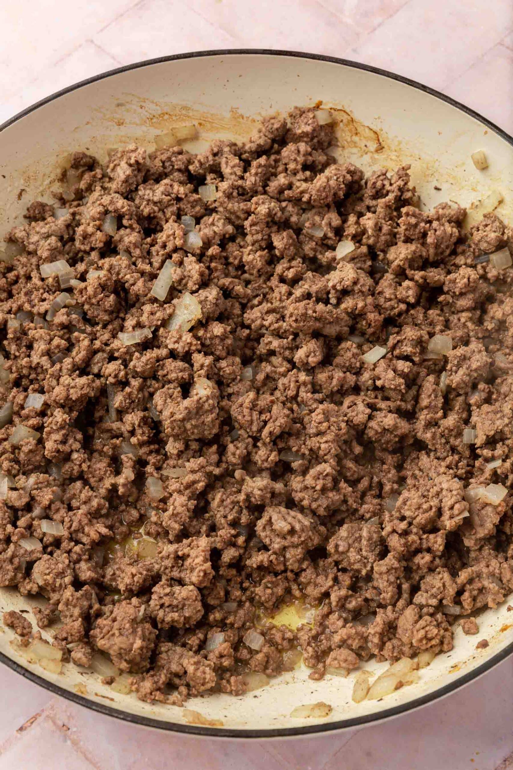 Cooked ground beef and diced onions in a round braising pan.