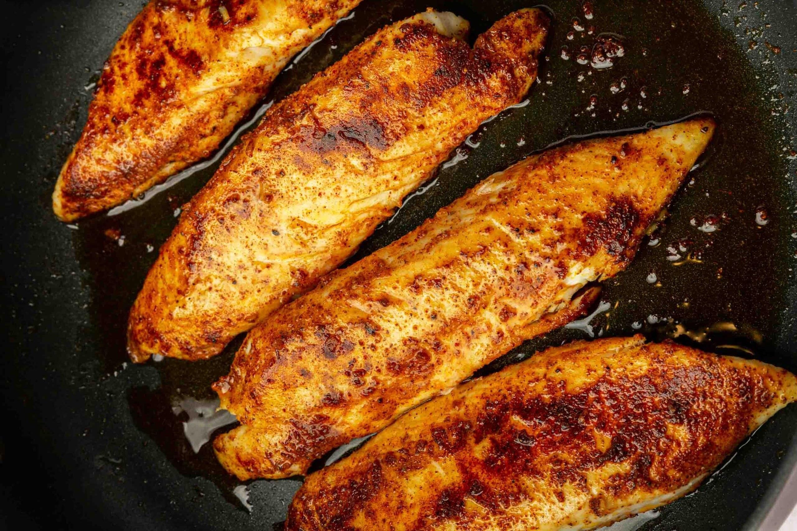 Four tilapia loin filets cooked in a non-stick skillet with oil.