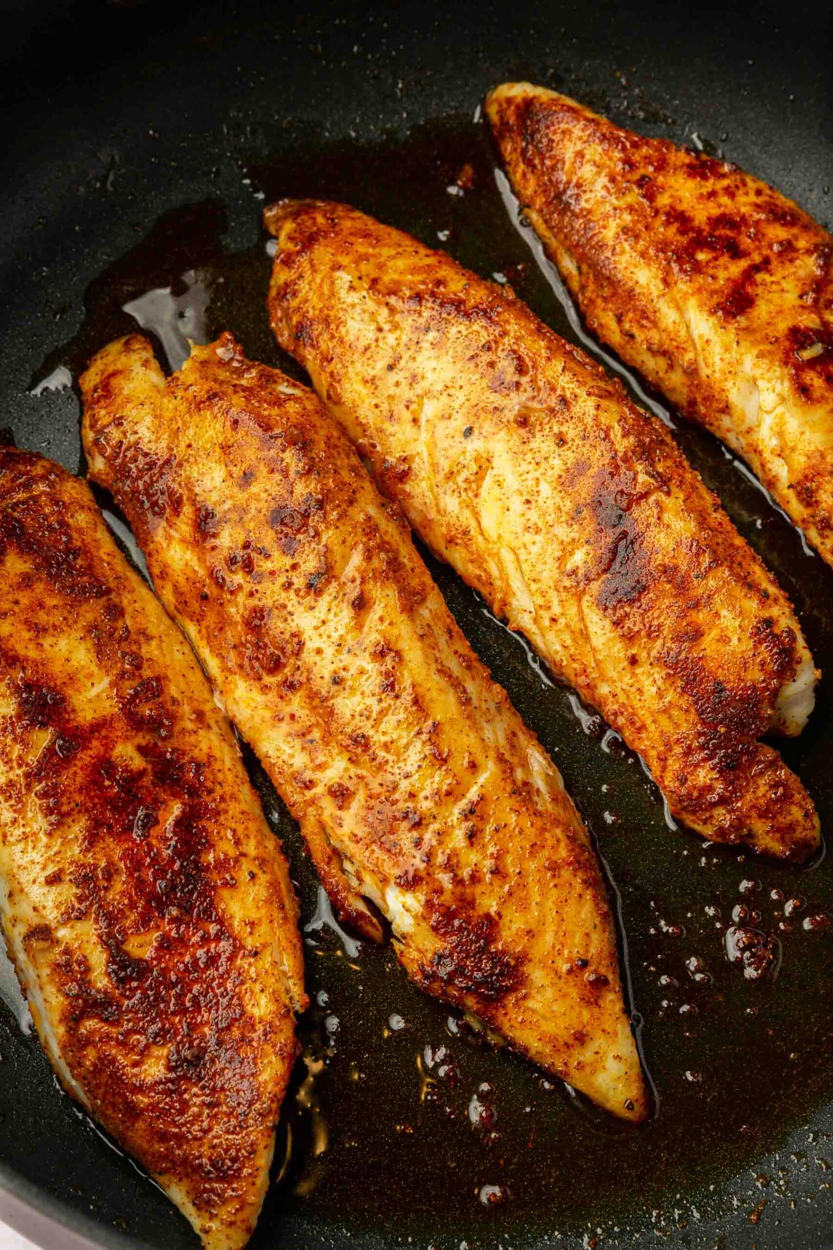 Four tilapia loin filets cooked in a non-stick skillet with oil.