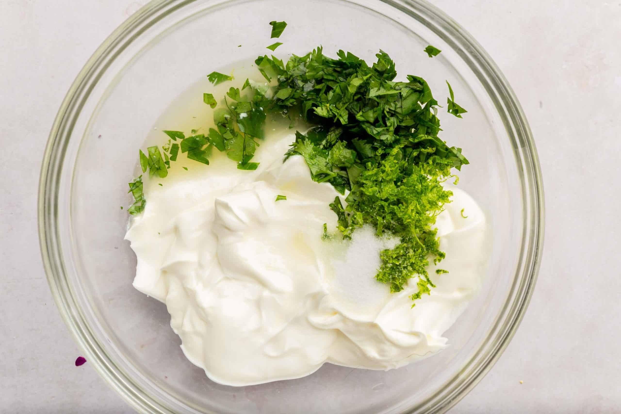 A glass mixing bowl with sour cream mixed with lime juice, lime zest, salt, and cilantro.