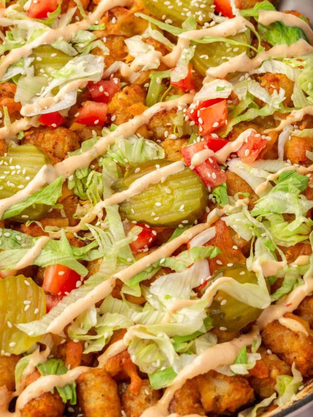 A close up of a big mac casserole with pickles, lettuce, tomatoes, and big mac sauce in a casserole dish.